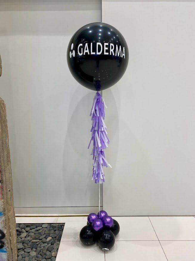A black balloon with the name galderma on it is surrounded by purple balloons.