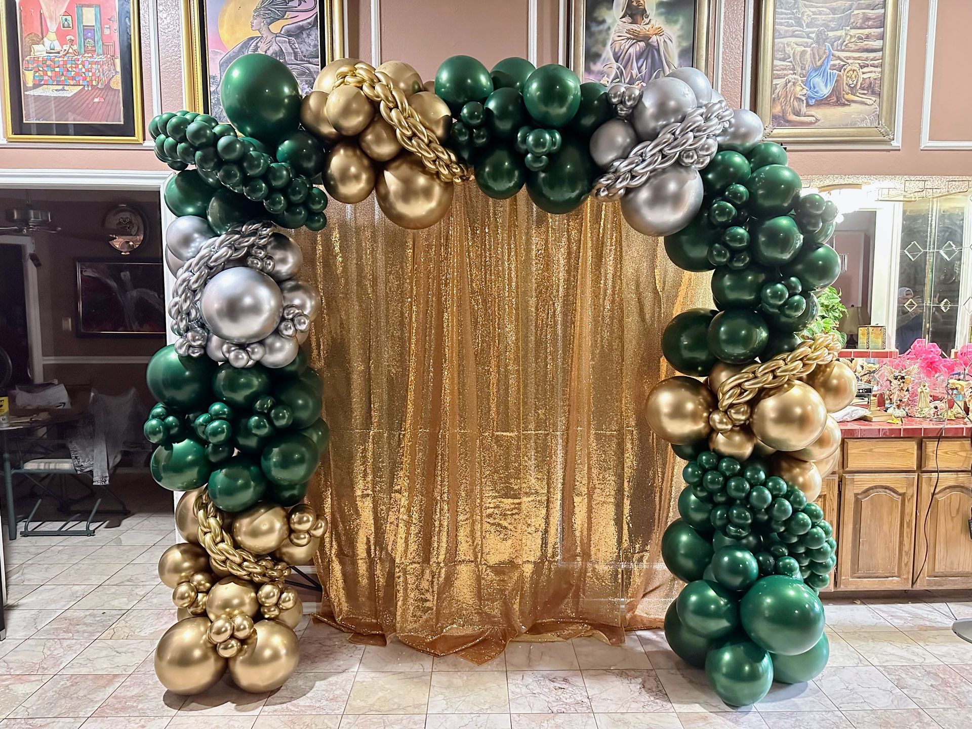 A room decorated with green and gold balloons and a gold curtain.