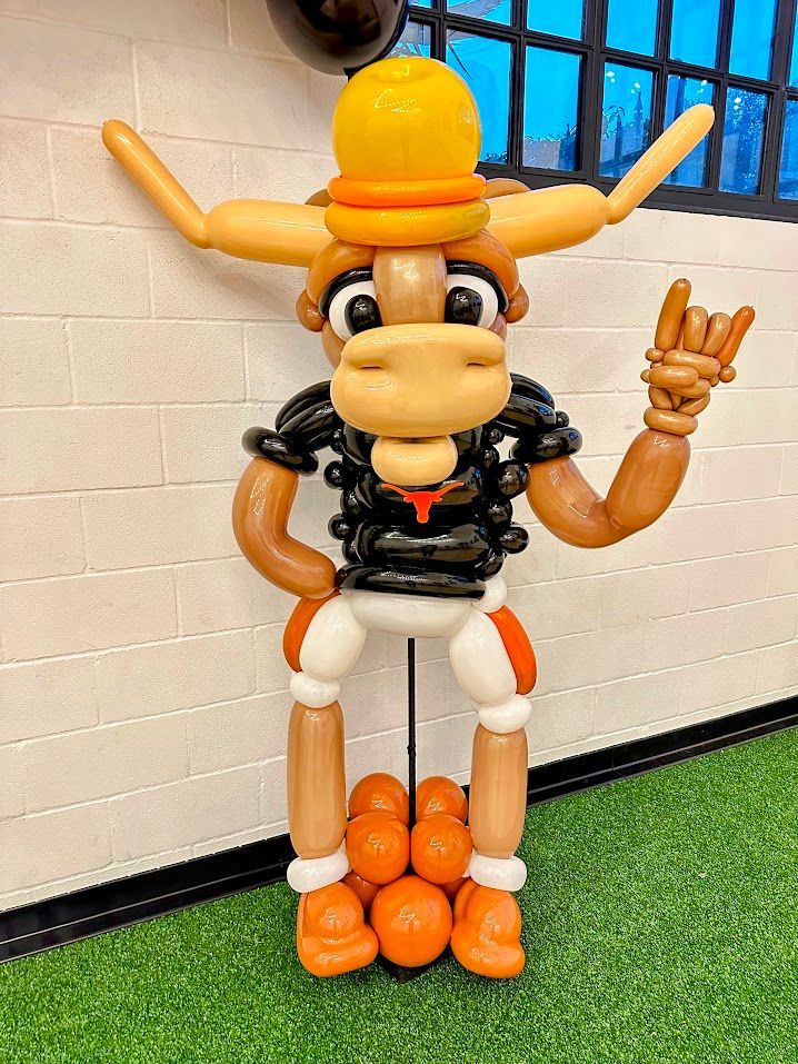 A bull made out of balloons is standing in front of a brick wall.