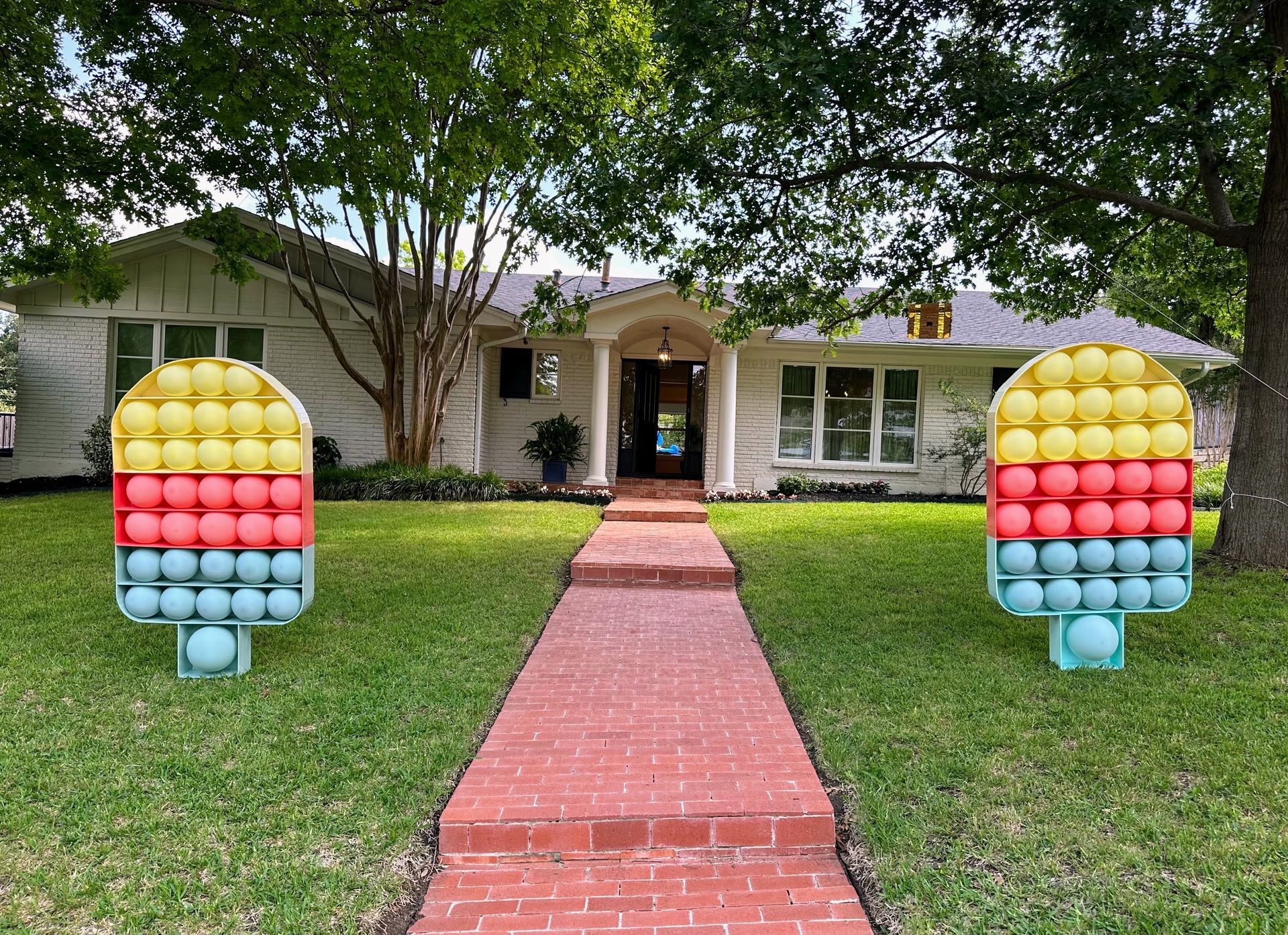 A house with a brick walkway and two pop it ice cream sculptures in front of it.