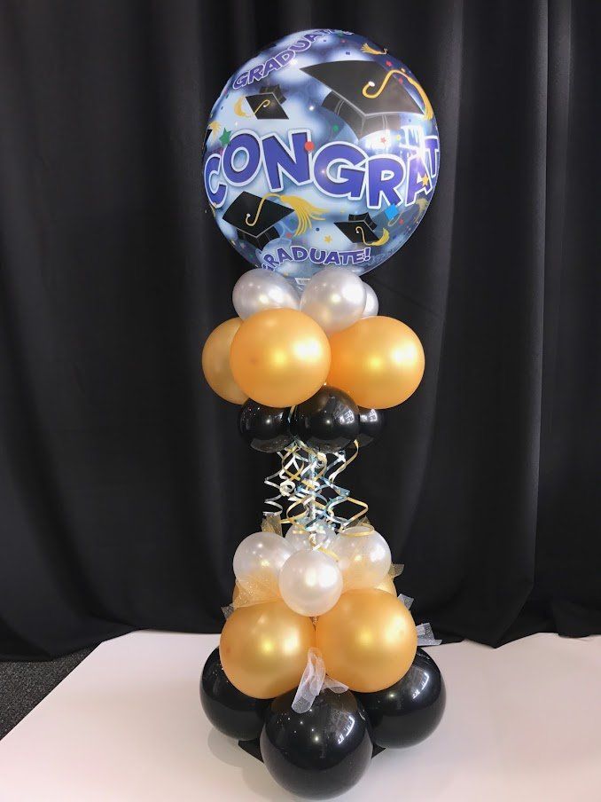 A congratulations balloon is surrounded by balloons on a table.