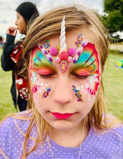 A little girl with her face painted like a unicorn.