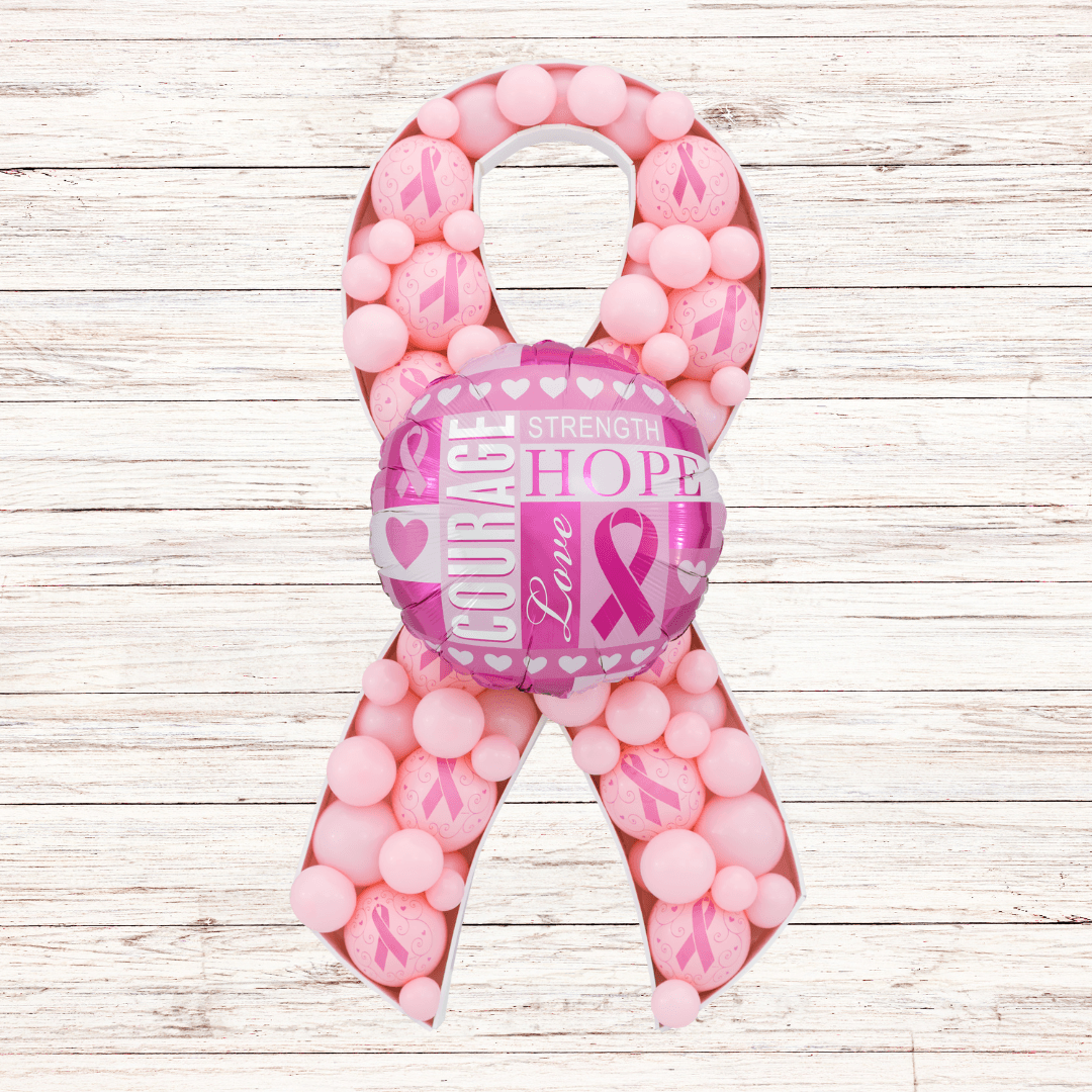 A pink ribbon is surrounded by pink balls on a white wooden table.