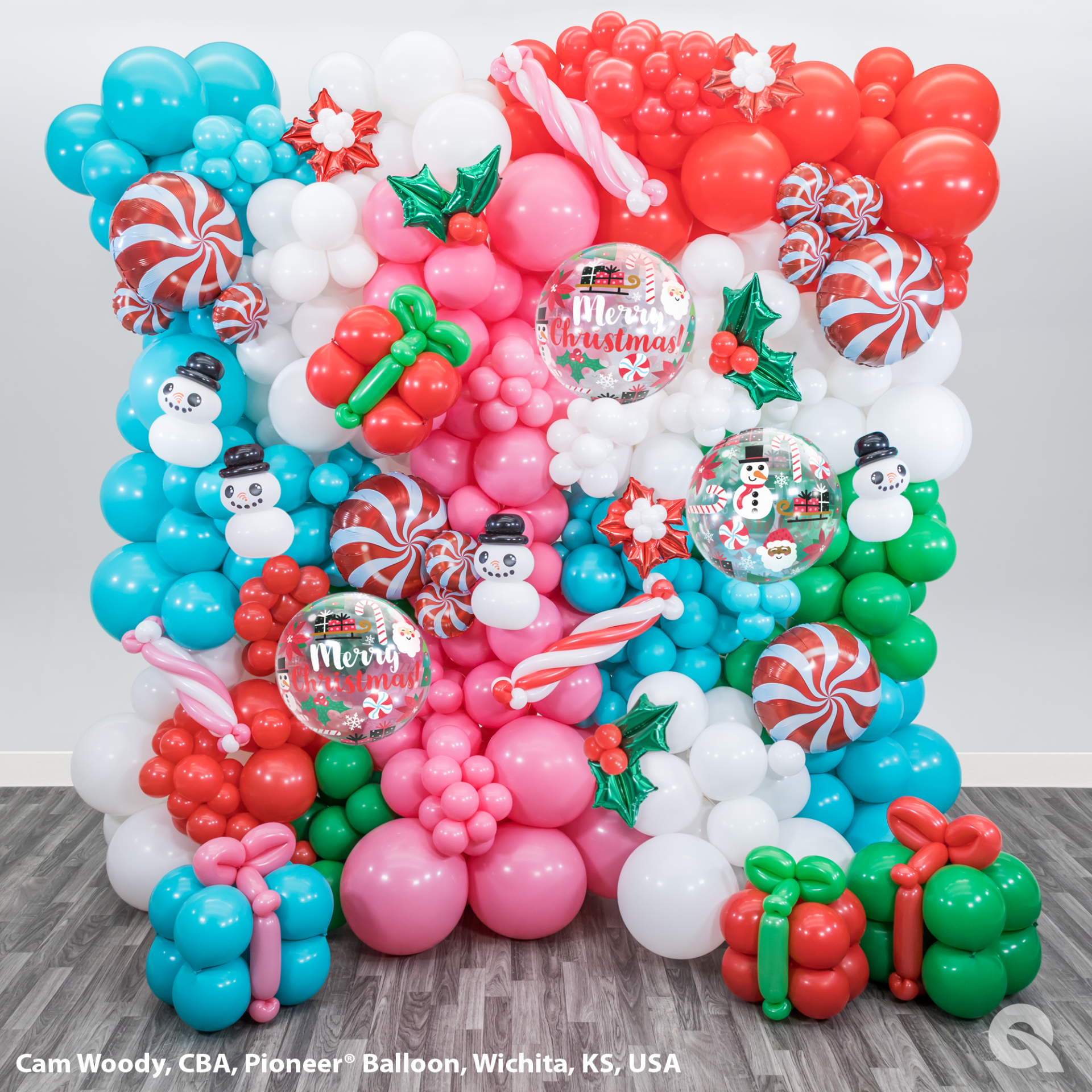 A wall of balloons decorated for christmas with snowmen , candy canes , and presents.