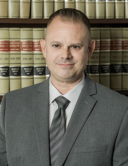 Man in a gray suit standing before law books in a library-like office