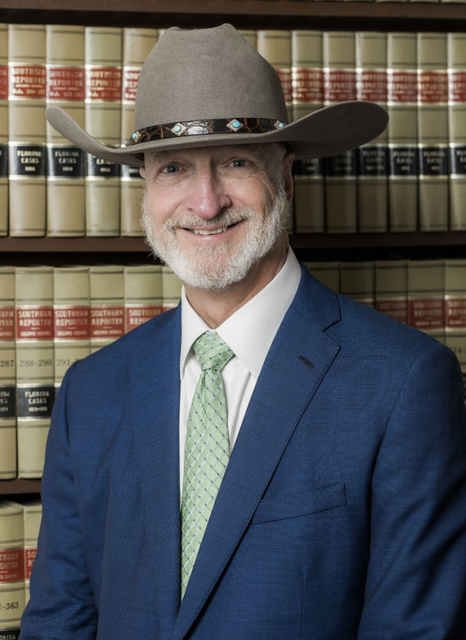 Man in blue suit and cowboy hat standing before shelves of law books, smiling