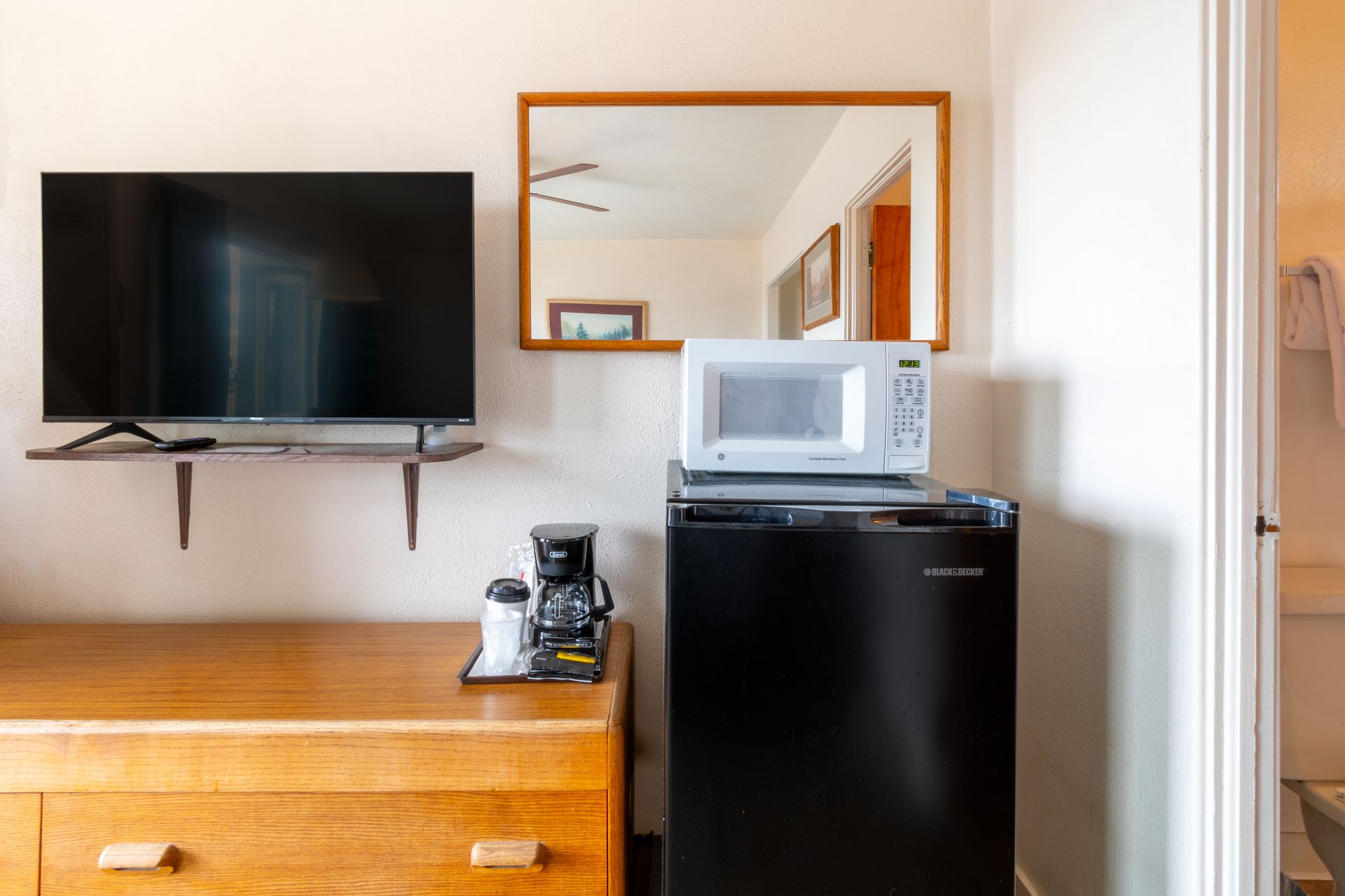 A hotel room with a dresser, mounted TV, mirror, mini-fridge, microwave, and coffee maker.