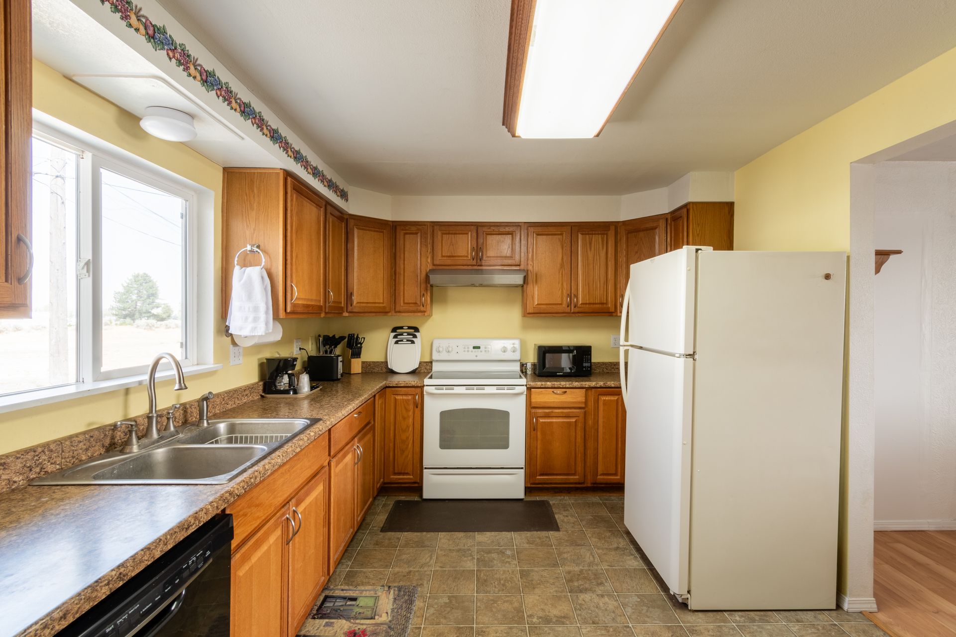 A kitchen with wood cabinets, yellow walls, and a white refrigerator. A window is above a stainless steel sink.