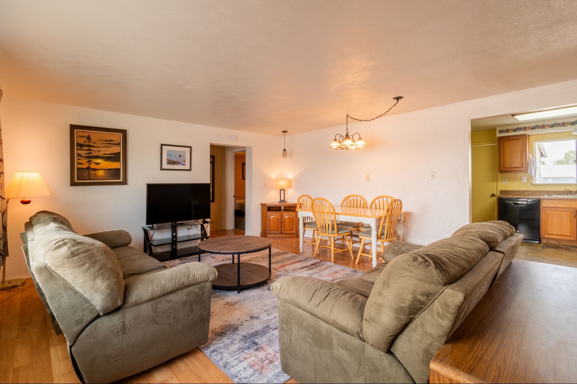 Cozy living room with two green couches, a dining table, and a view of a kitchen.