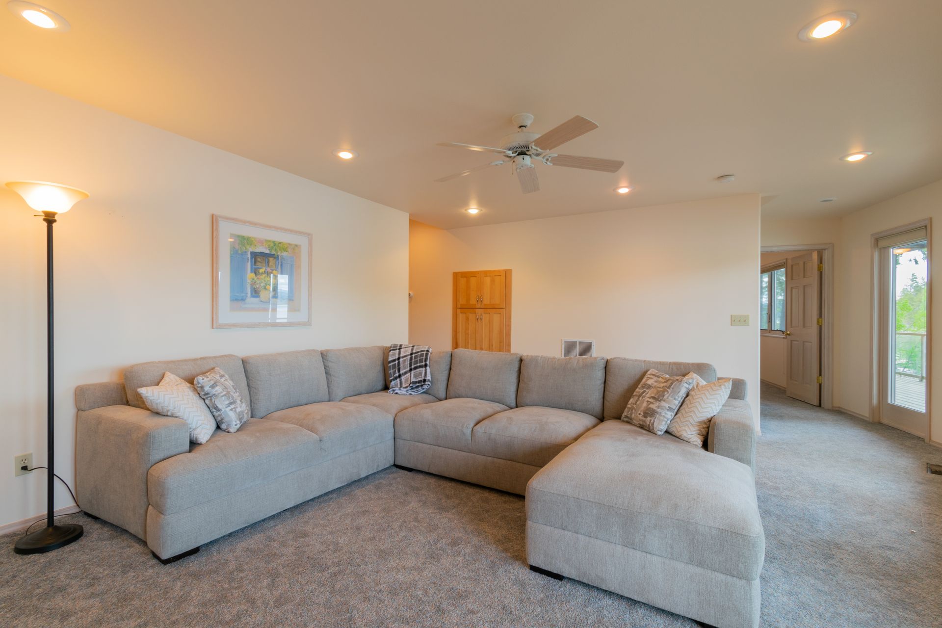 A large, light gray sectional sofa in a spacious living room with a fluffy carpet.