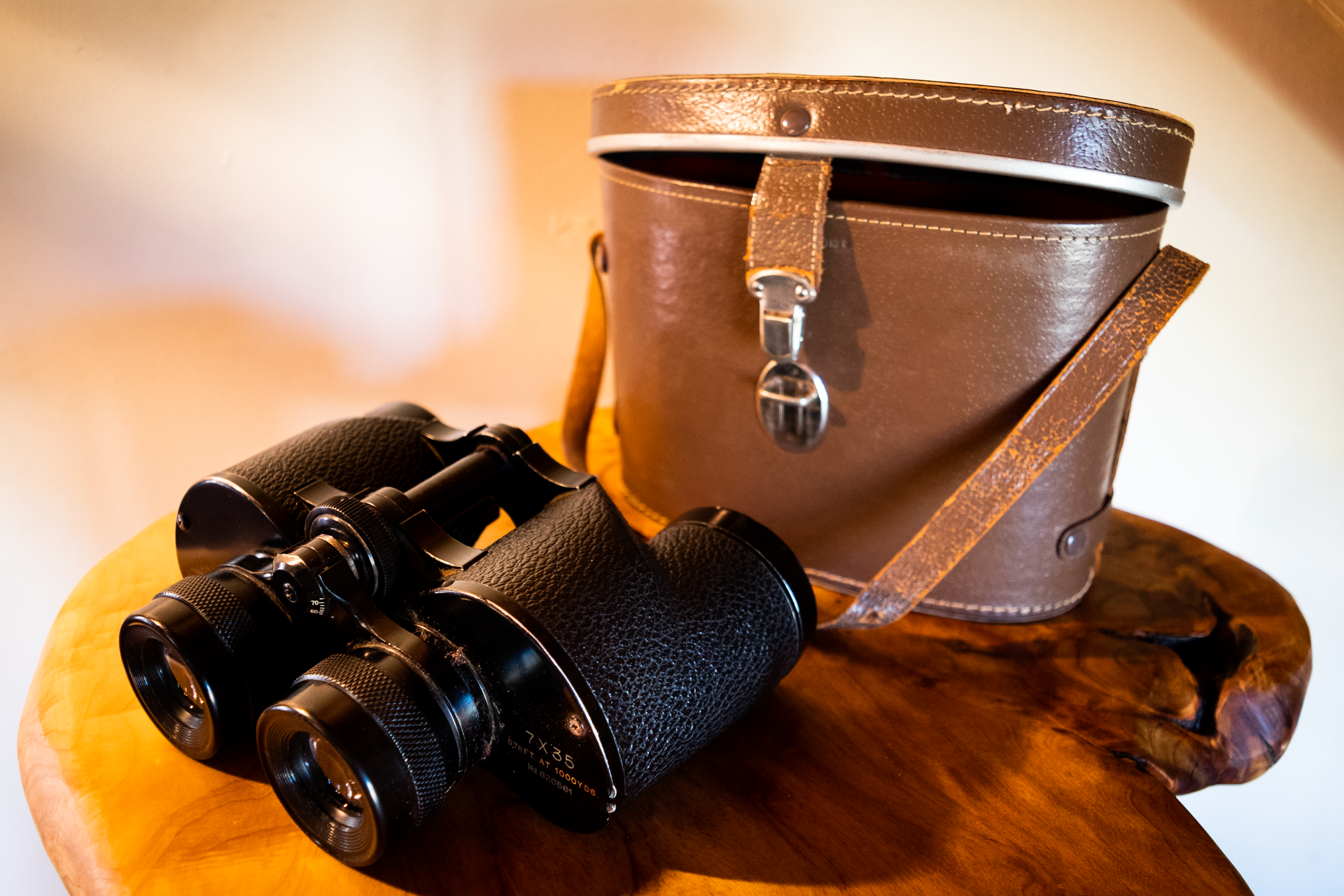 Binoculars and leather case sit on a wooden surface. Brown and black tones are prominent.