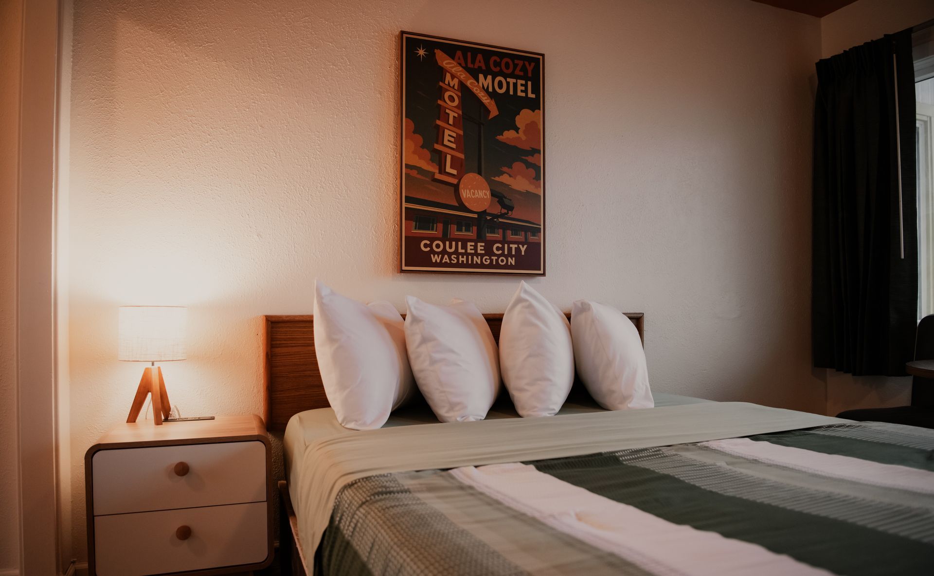 Bedroom interior with a bed, nightstand, lamp, and framed vintage poster.