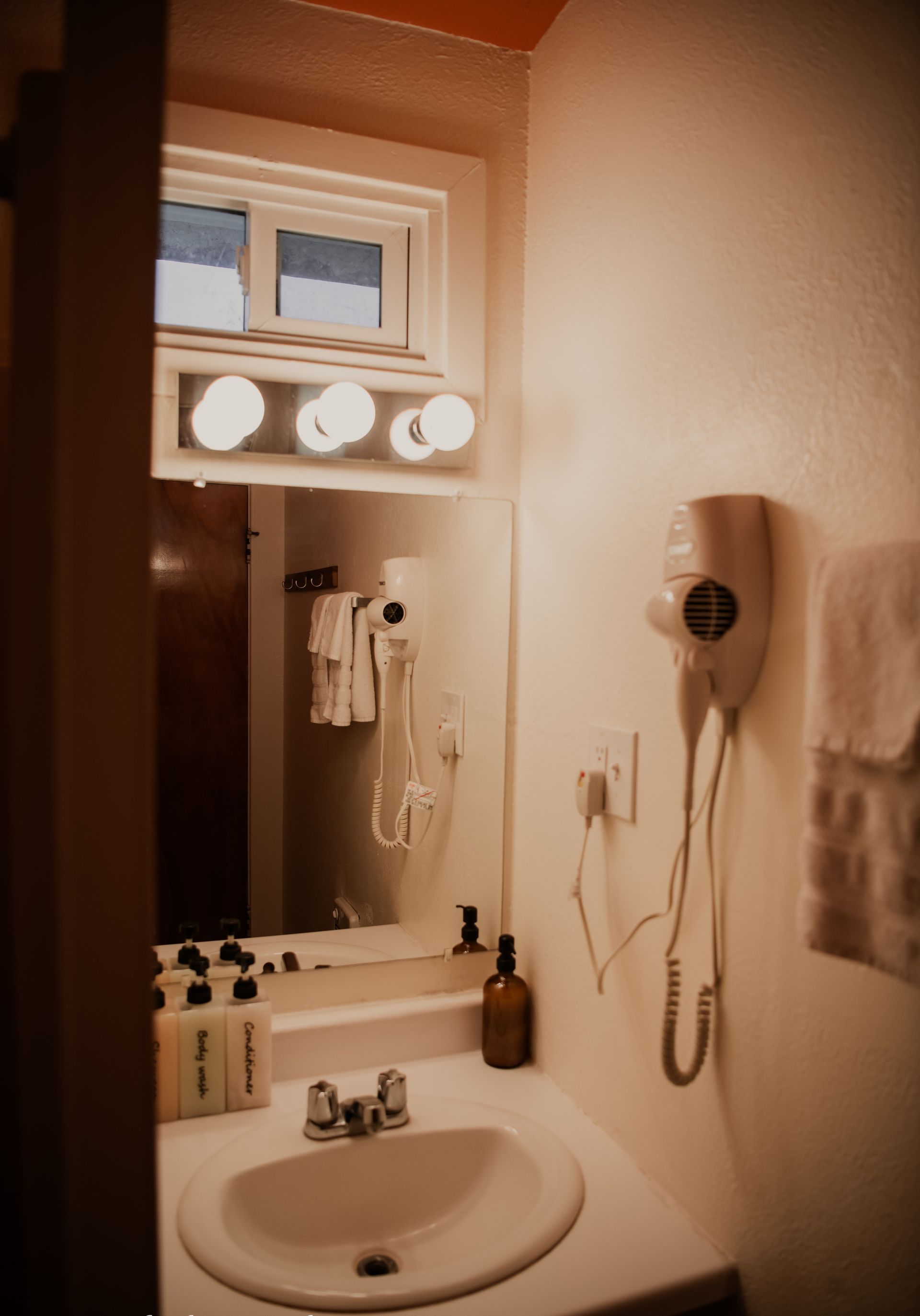 Small bathroom with a sink, mirror, and a wall-mounted hairdryer.  A small window is above the mirror.