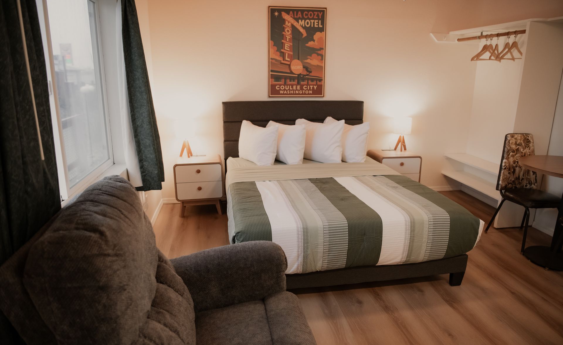 Bedroom with bed, nightstands, chair, and art; green and white bedding, grey walls, wooden floor.