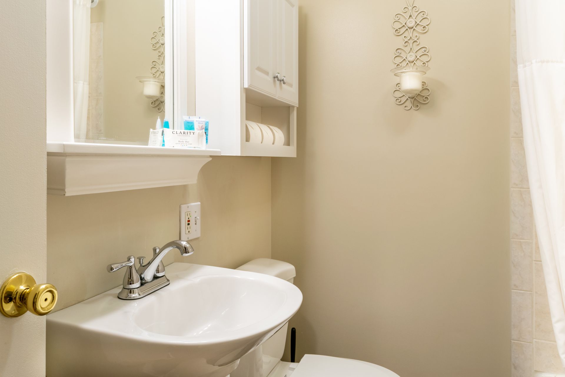 Small bathroom with white sink, toilet, and cabinet. A decorative candle holder hangs on the wall.