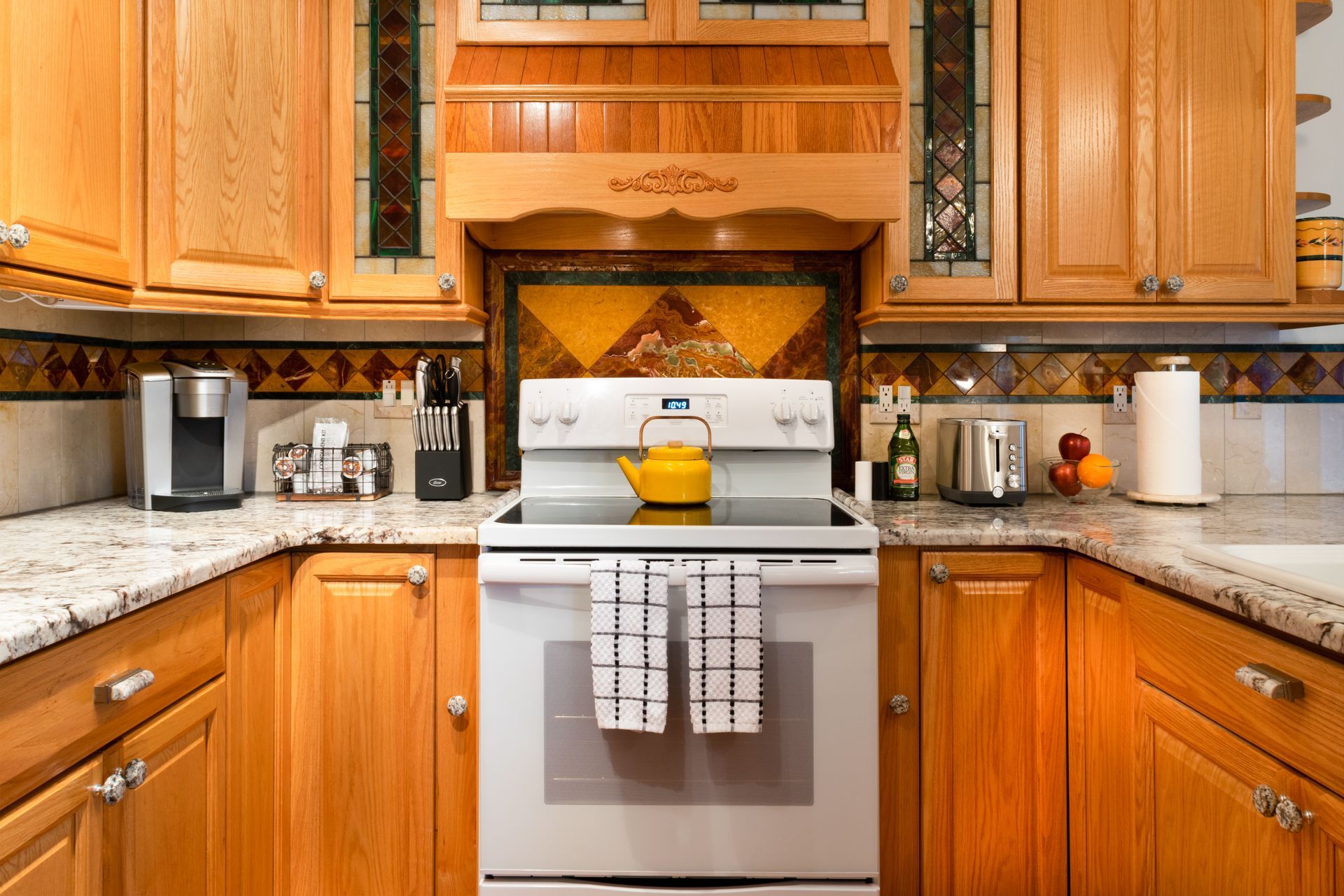 Kitchen with light wood cabinets, granite countertops, and a white stove with a yellow teapot.