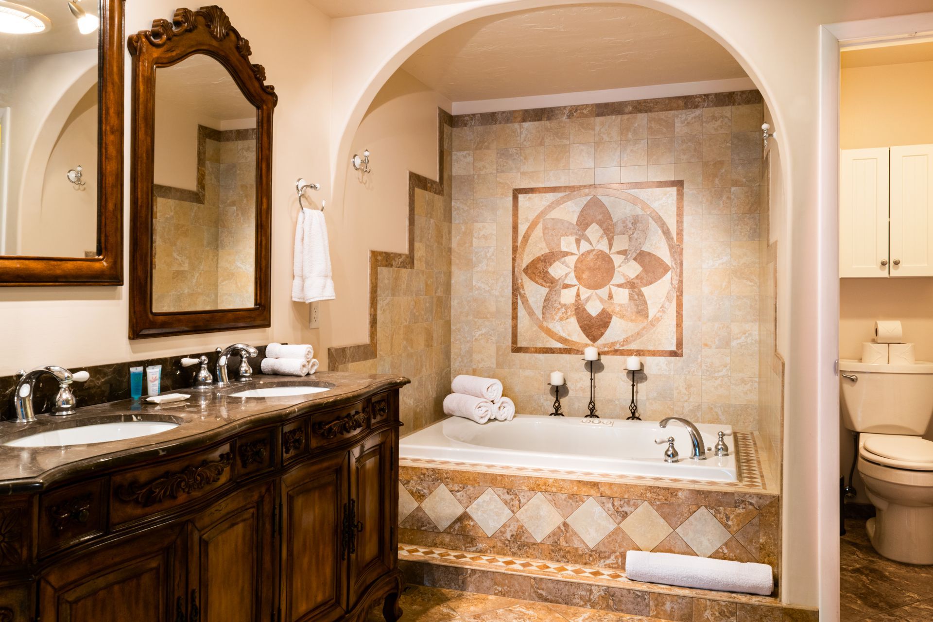 A luxury bathroom with dark wood vanity, large mirror, a raised tile bathtub, and decorative wall tile in earth tones.