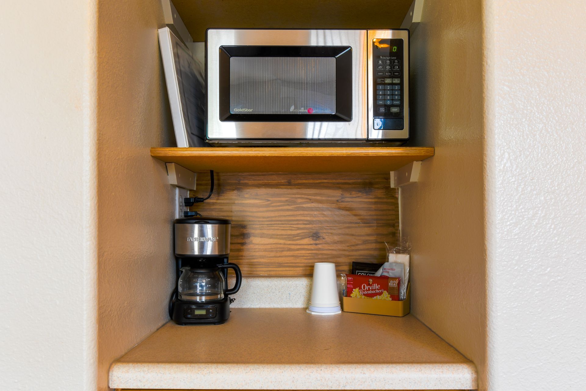 A small kitchen nook with a microwave on a shelf above a coffee maker. A cup and tissues are on the counter.