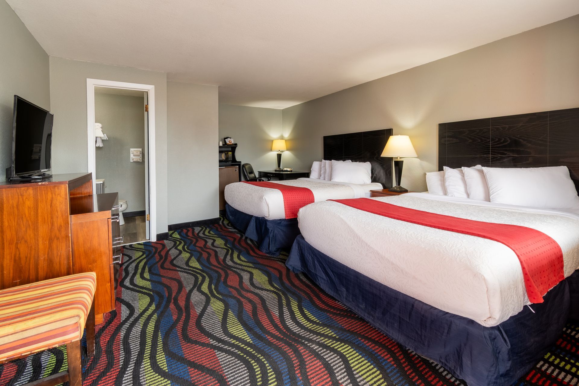 A motel room featuring a bed, dresser, table, and an open doorway to the bathroom.