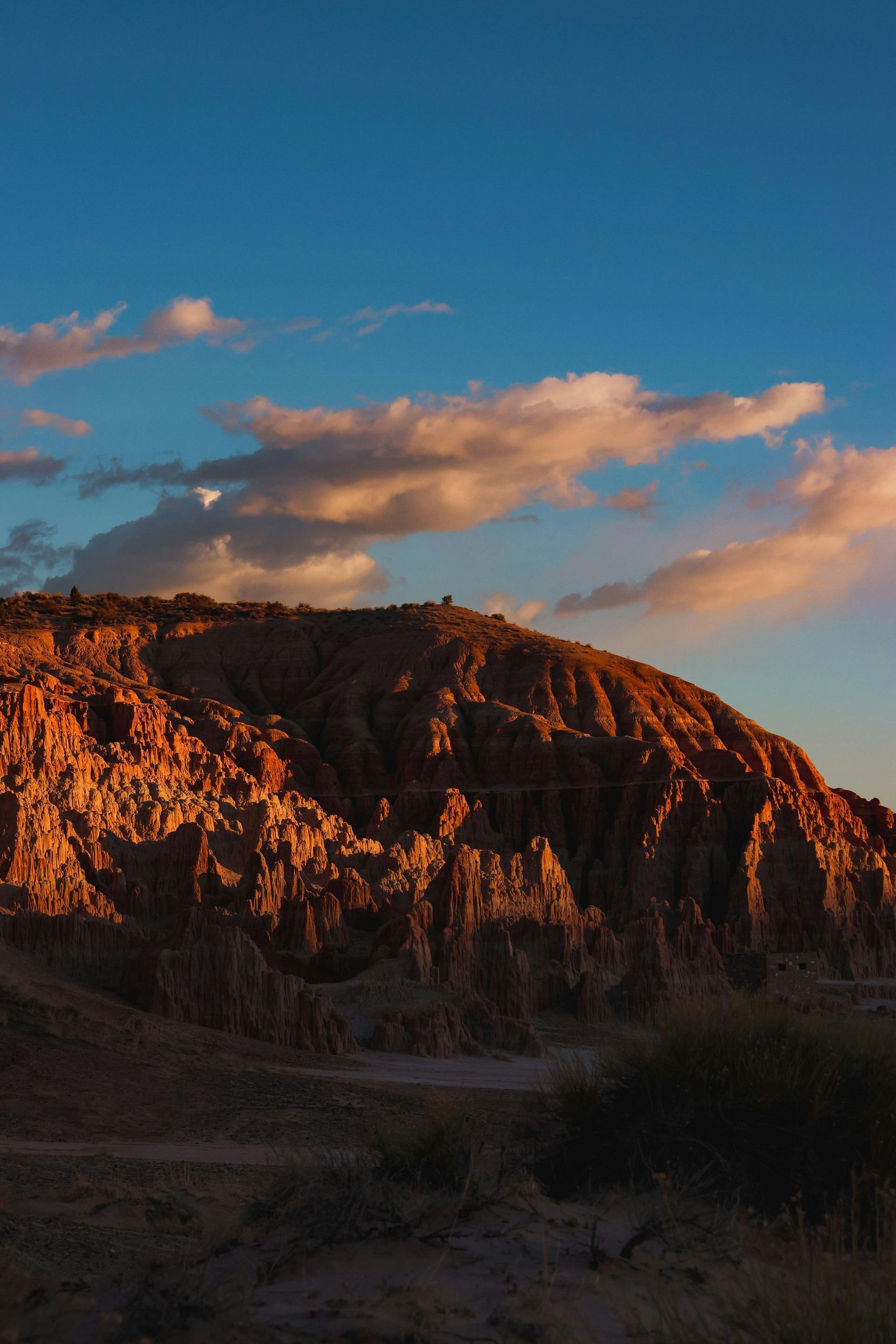 A rugged, sunlit mesa glows under a blue sky with fluffy clouds.