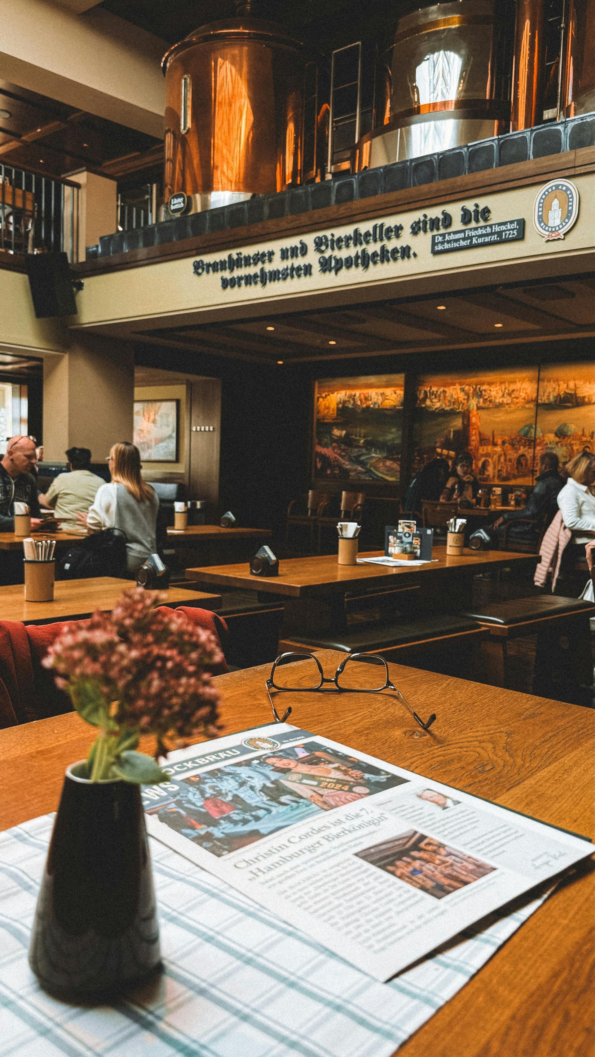 A table in a traditional German beer hall, with a newspaper and flowers in the foreground.