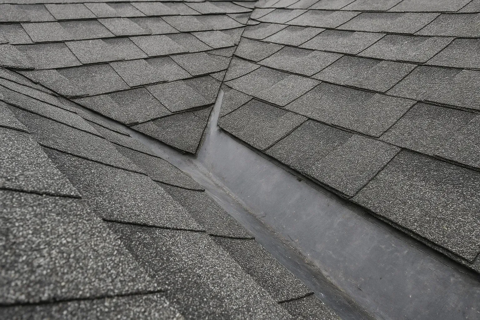 Damaged asphalt roof shingles with a long gap and exposed underlayment in the center
