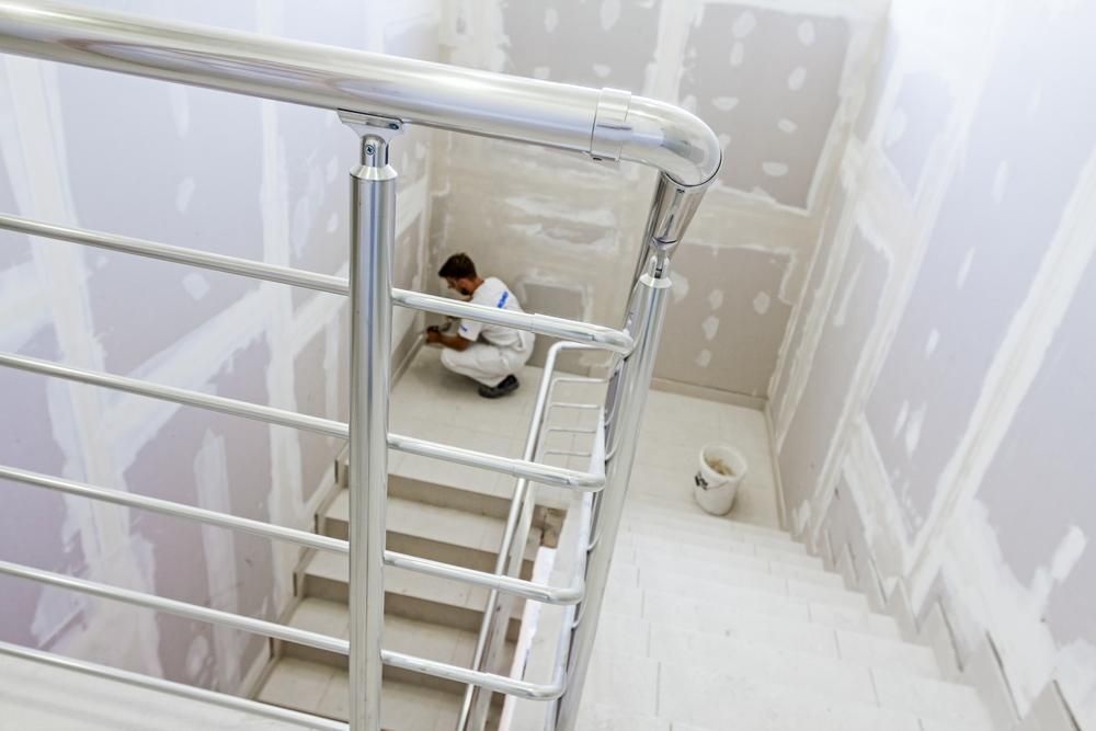 A Man is Kneeling on the Floor in a Room Next to a Staircase — Kymar Steel Fabrications in Teralba, NSW