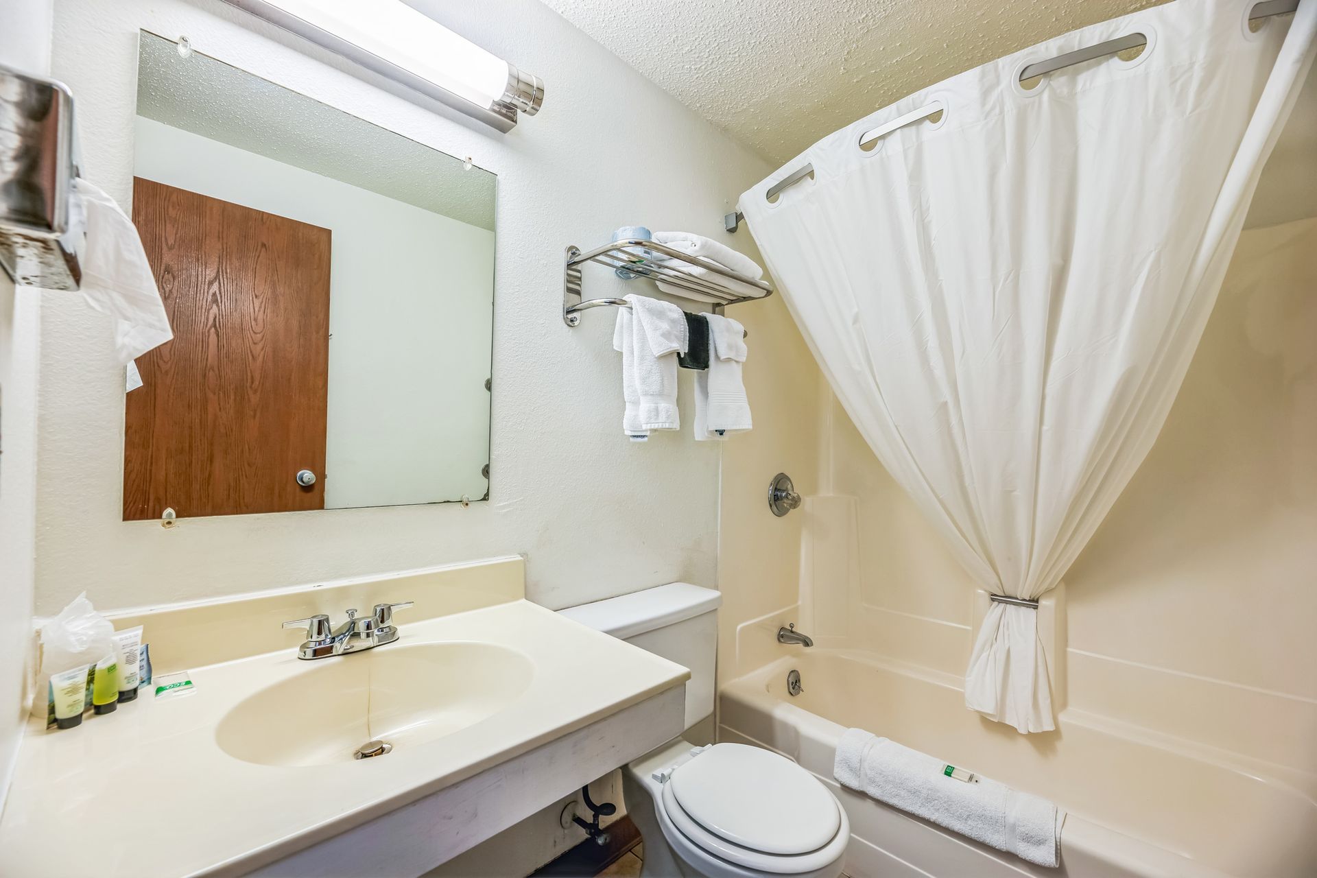 Bathroom with white sink, toilet, and bathtub. Shower curtain drawn. Light fixture above mirror.