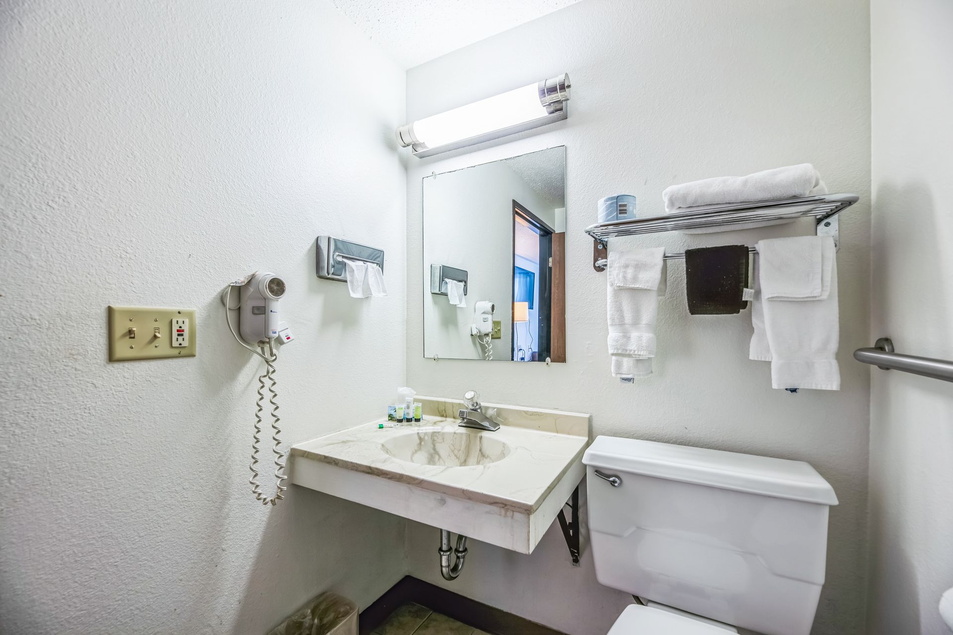 Bathroom with a sink, mirror, toilet, towel rack, and hairdryer. White walls and fixtures.