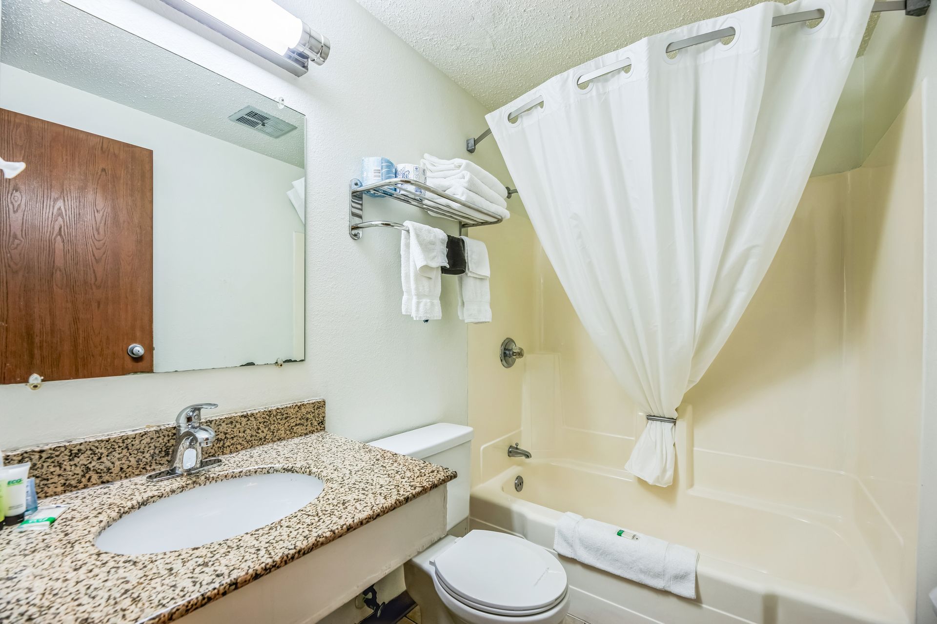 Bathroom with a sink, toilet, and bathtub/shower. Beige walls and a white shower curtain.