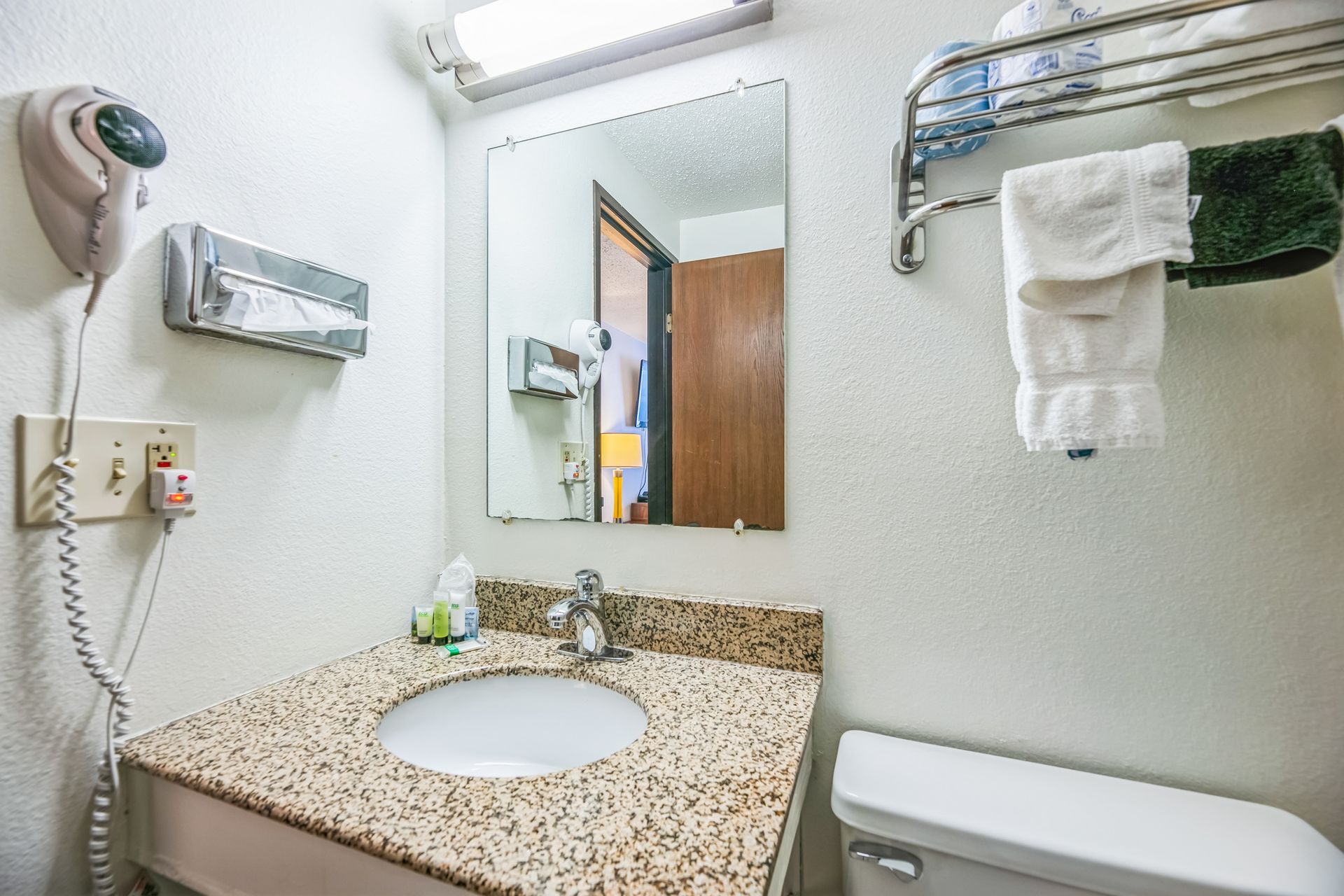 Bathroom sink with mirror, hairdryer, towels, and toilet.