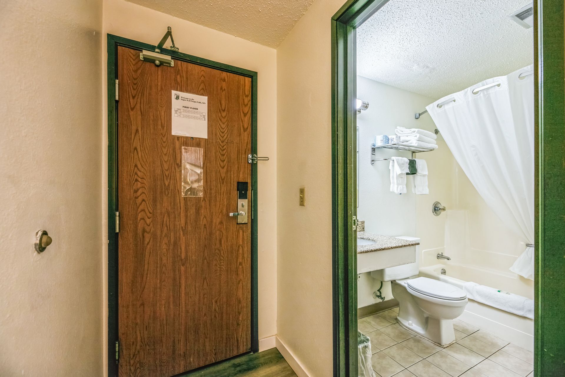 Interior hotel room entryway with a wooden door and an open bathroom door.