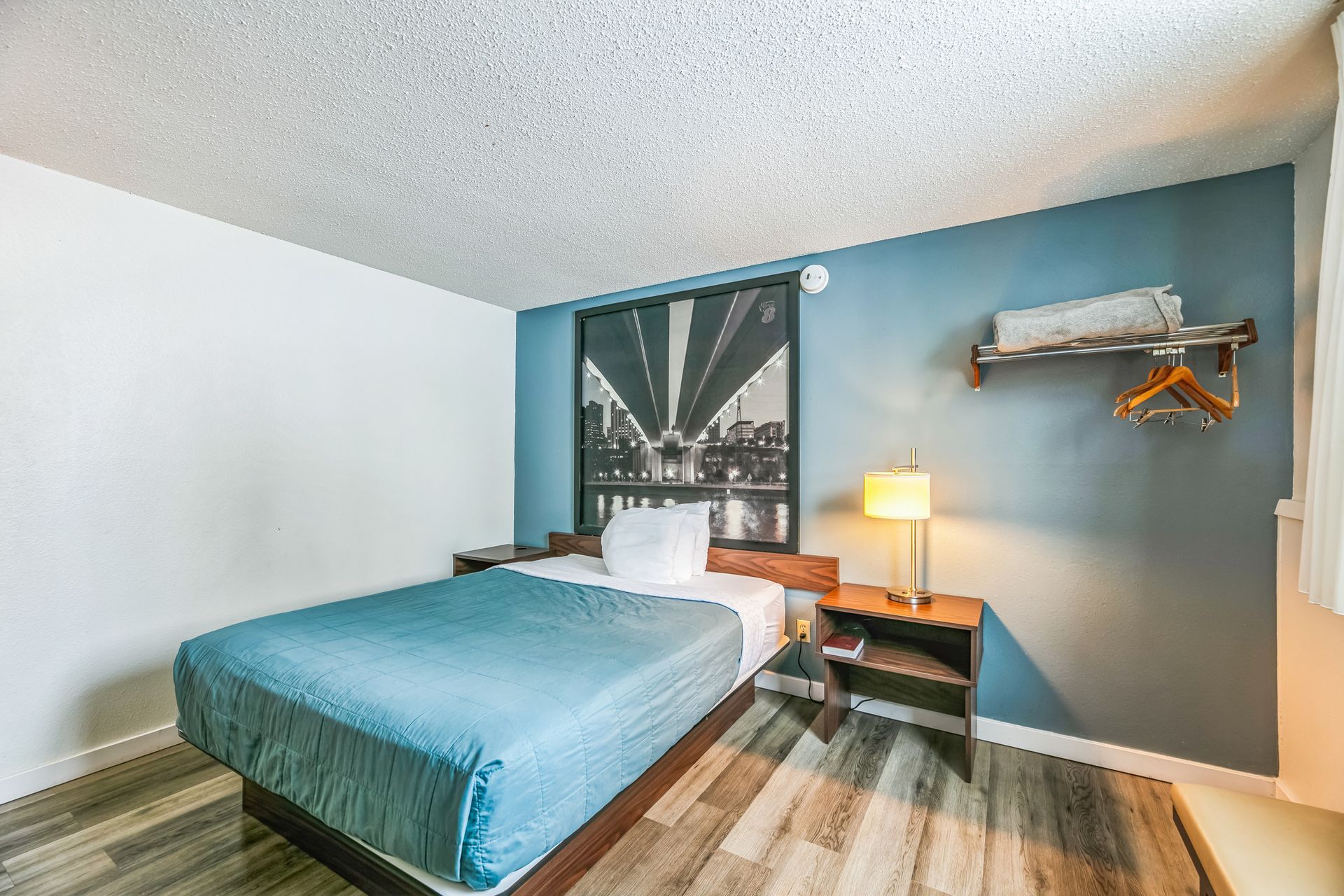 Bedroom with bed, nightstand, shelf, and art on a blue wall.