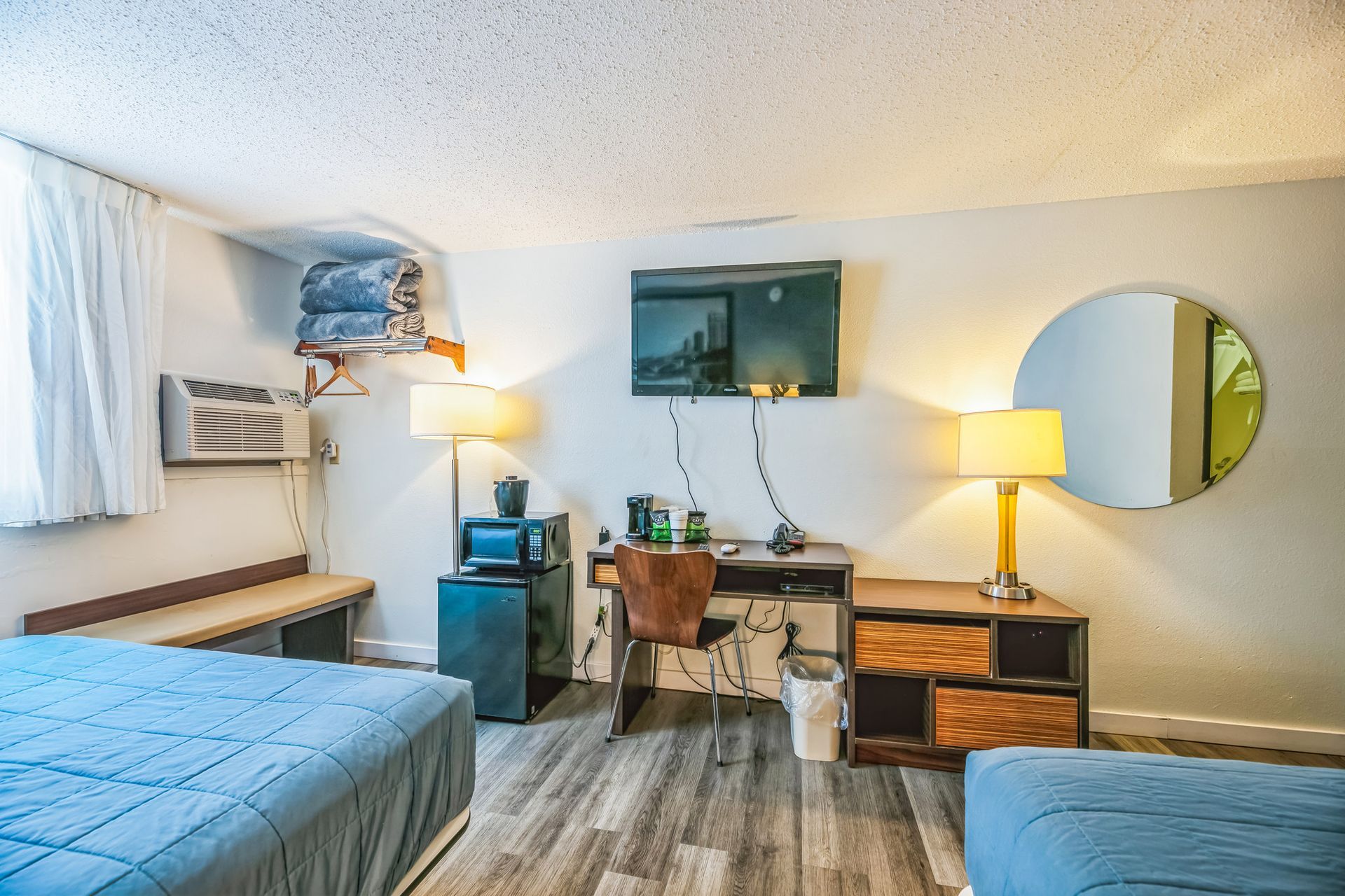 Hotel room with two beds, desk, TV, microwave, and round mirror.