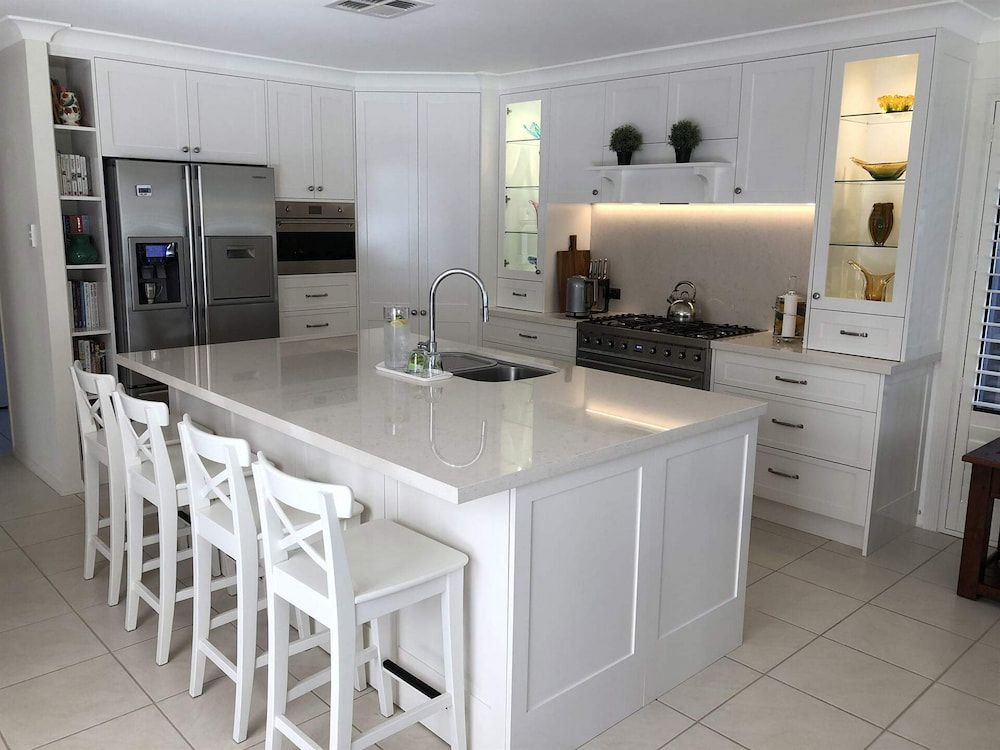 A Kitchen With White Cabinets And Stools And A Large Island — Cross Cabinets In Chevallum, QLD