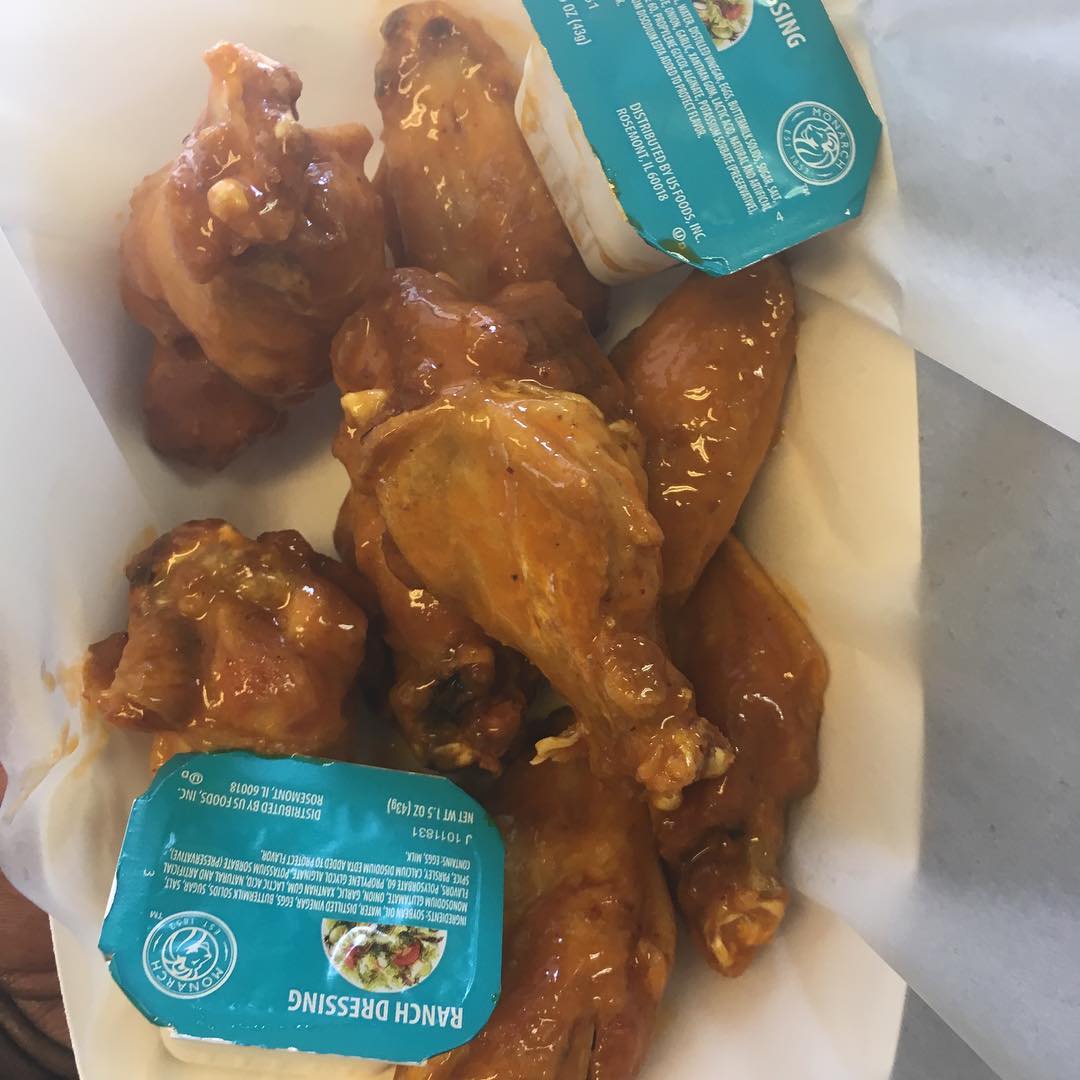 Chicken wings with sauce and ranch dressing in a white container.