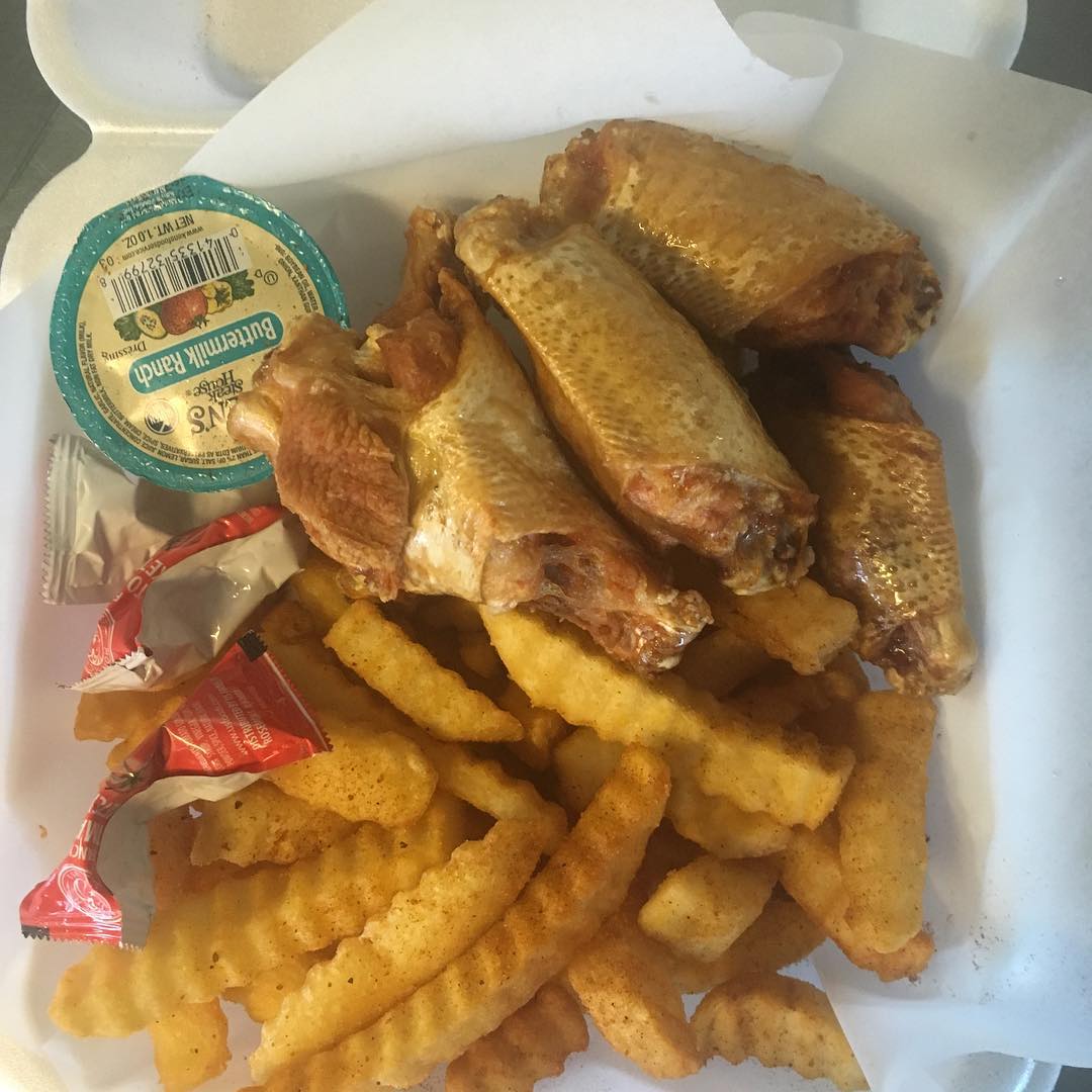 Chicken wings, crinkle-cut fries, ranch dressing, and ketchup in a white takeout container.