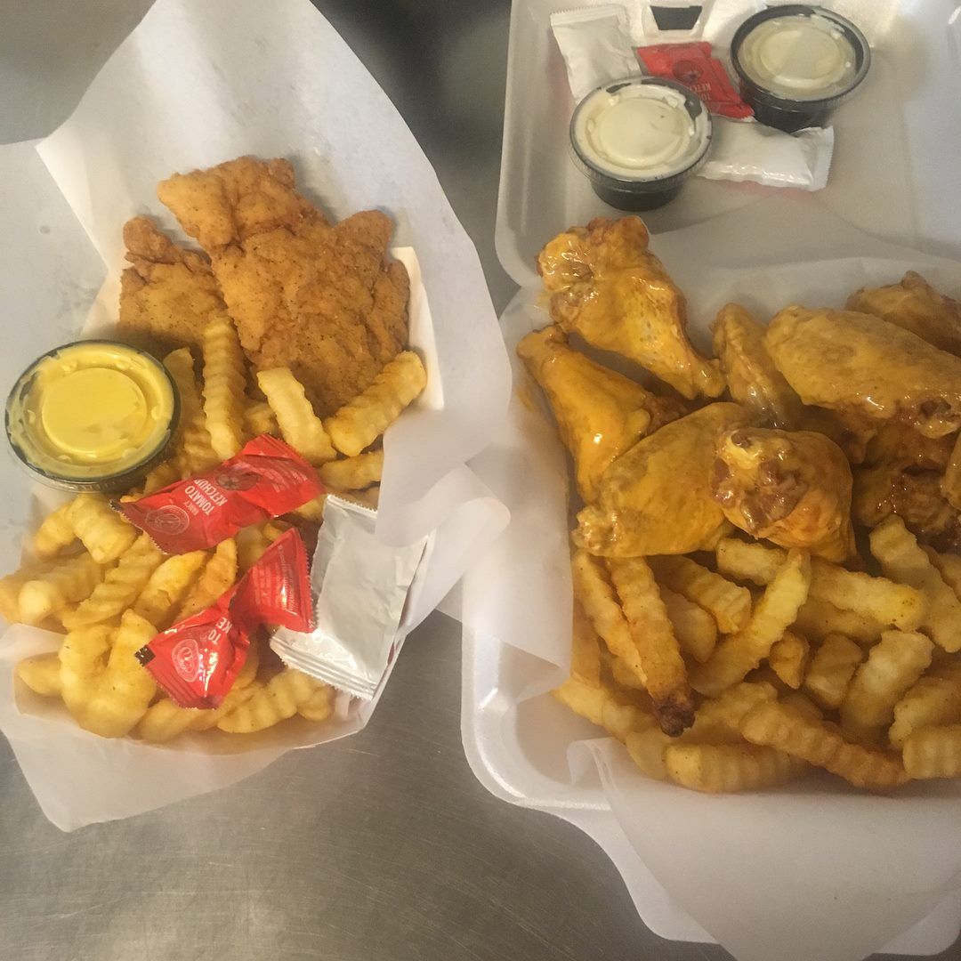 Chicken strips and wings with fries and dipping sauces in take-out containers.
