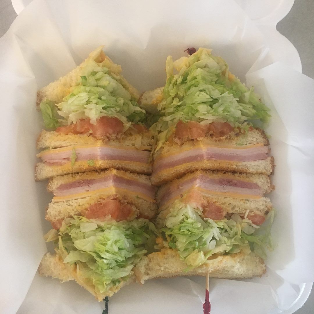 Club sandwich on white bread with lettuce, tomato, ham, and cheese, cut into four triangles.