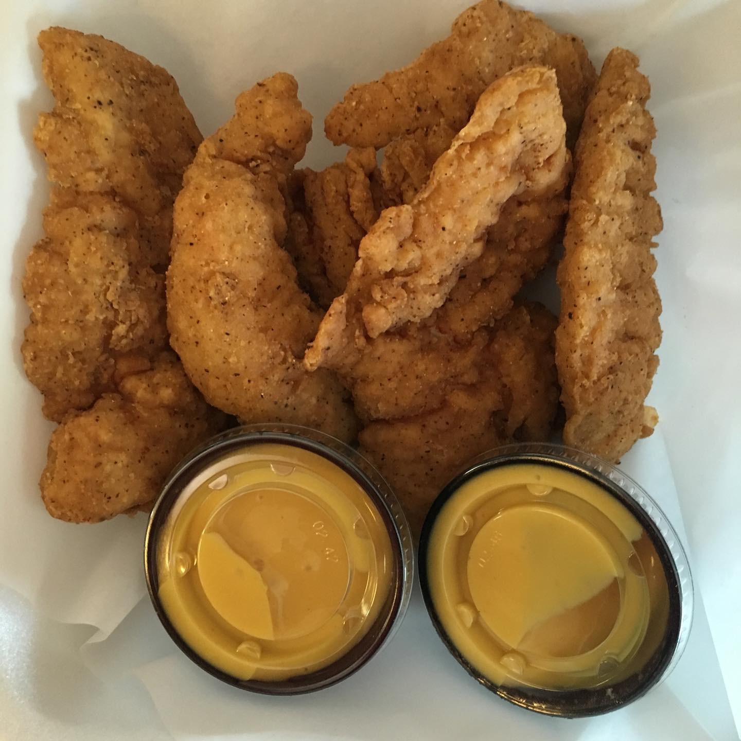 Fried chicken tenders with two small containers of yellow dipping sauce.
