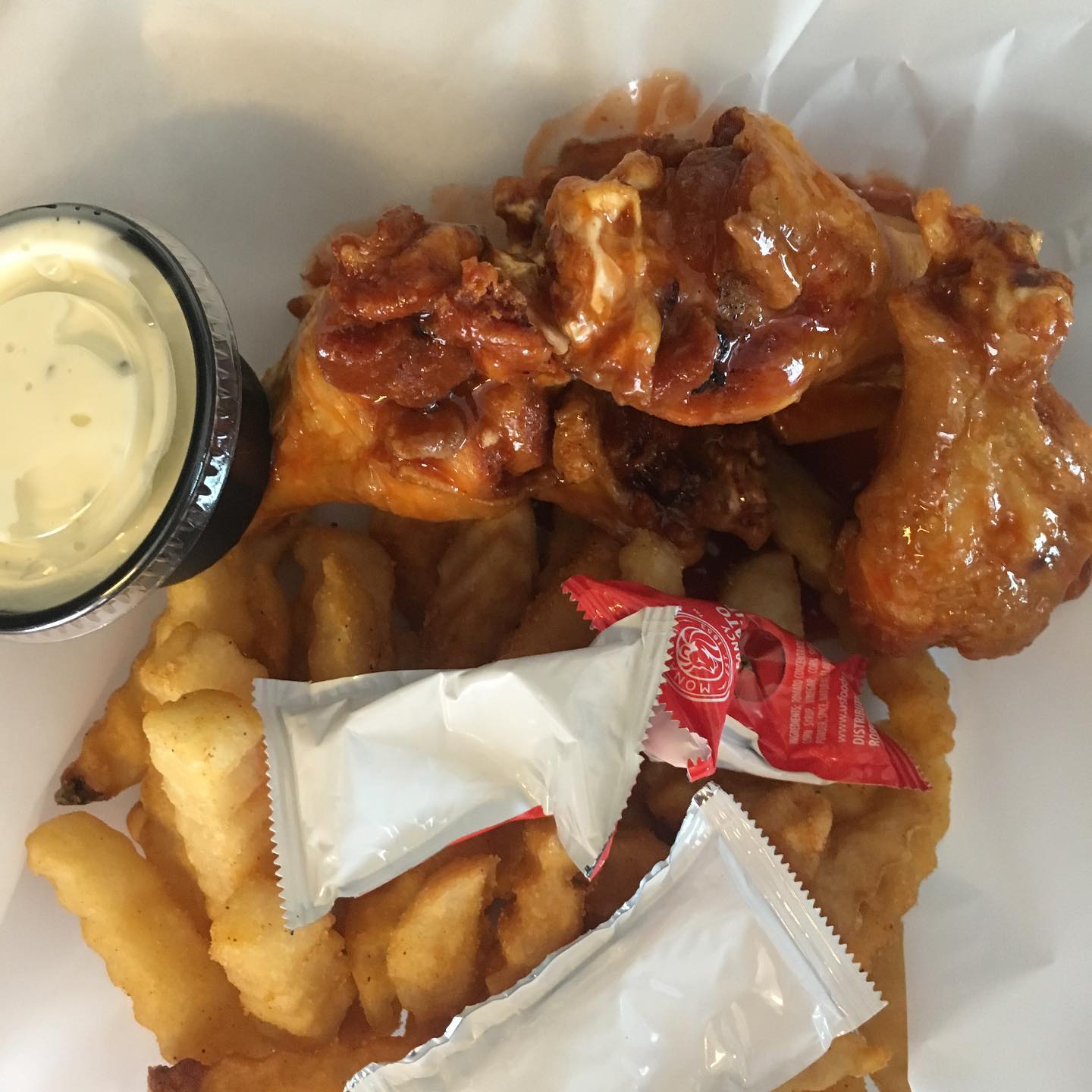 Chicken wings, fries, and sauce in a white takeout container.