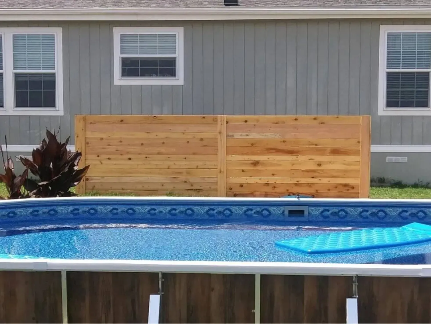 A swimming pool in front of a house with a wooden fence