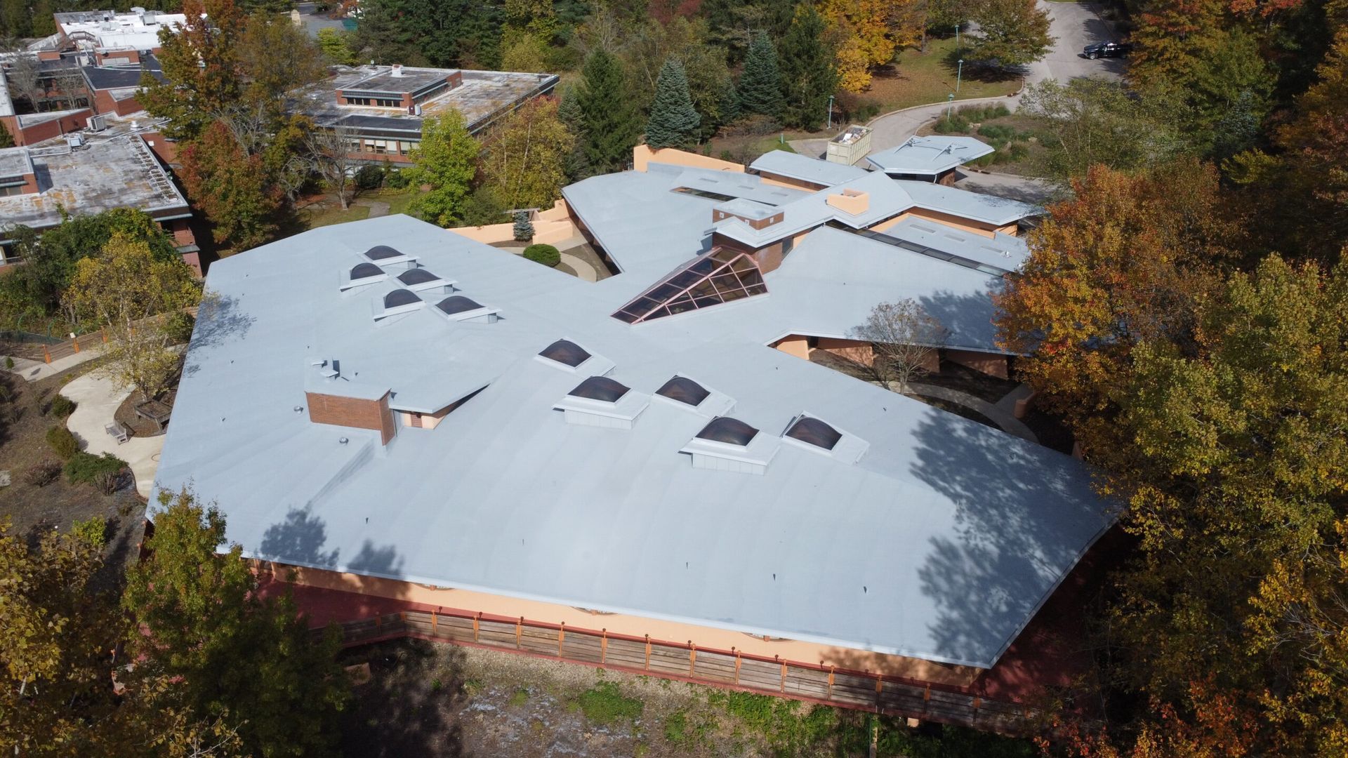 Aerial view of a building with a damaged white roof surrounded by trees and houses.