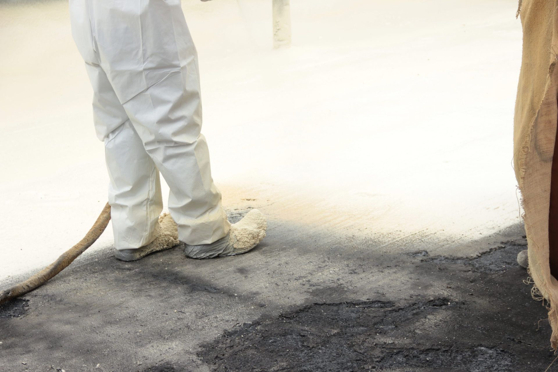Worker in white protective suit standing beside a dark paved area near a wall.