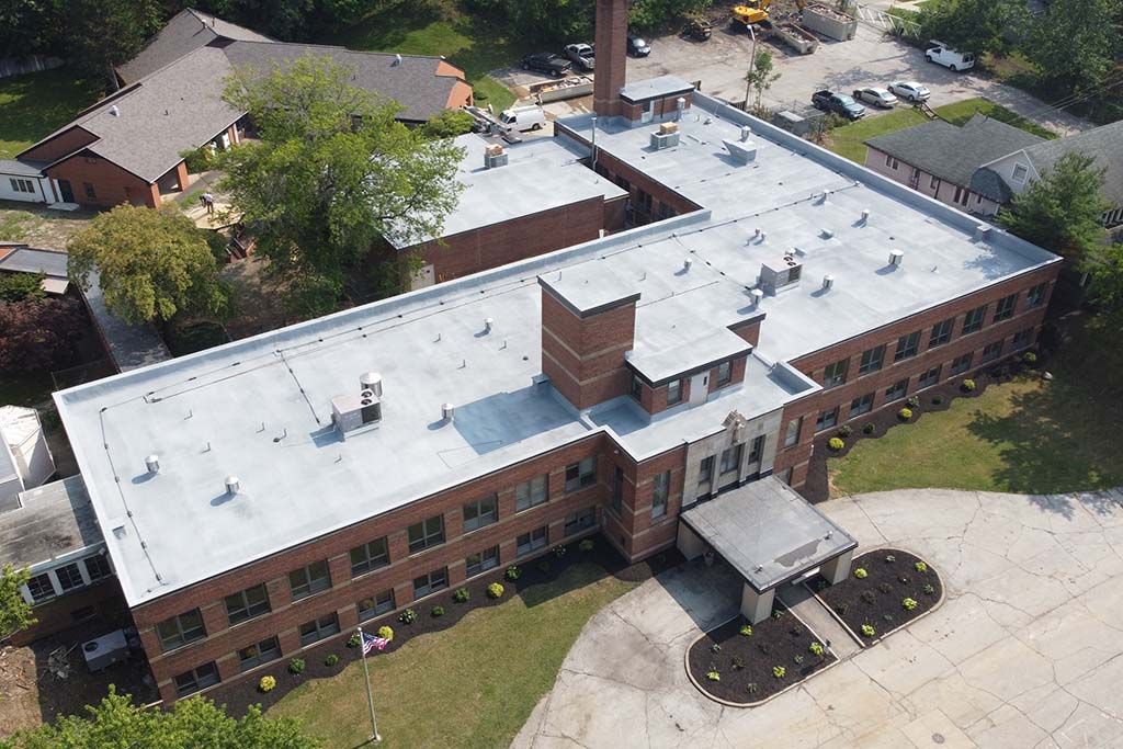 Aerial view of a brick building with a white roof, surrounded by trees and a parking area.