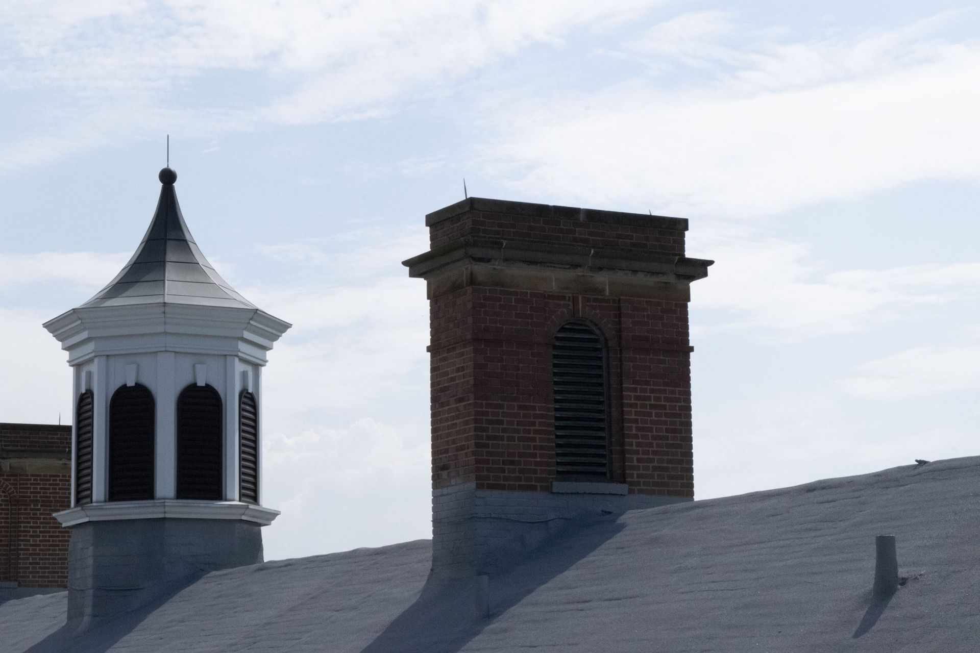 Two rooftop chimneys against a pale sky, one white cupola and one brick tower