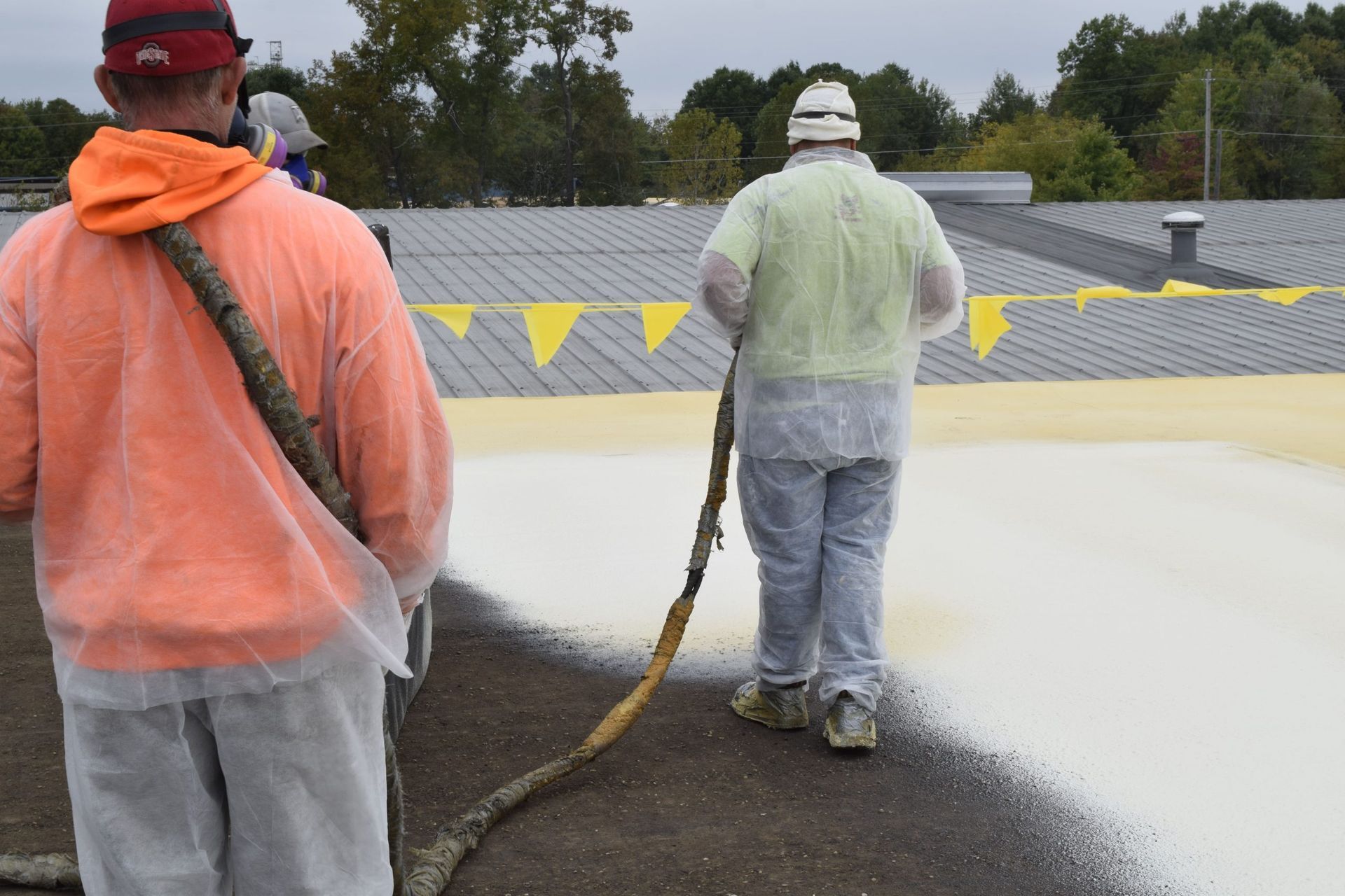 Workers spraying white coating on a roof under cloudy skies