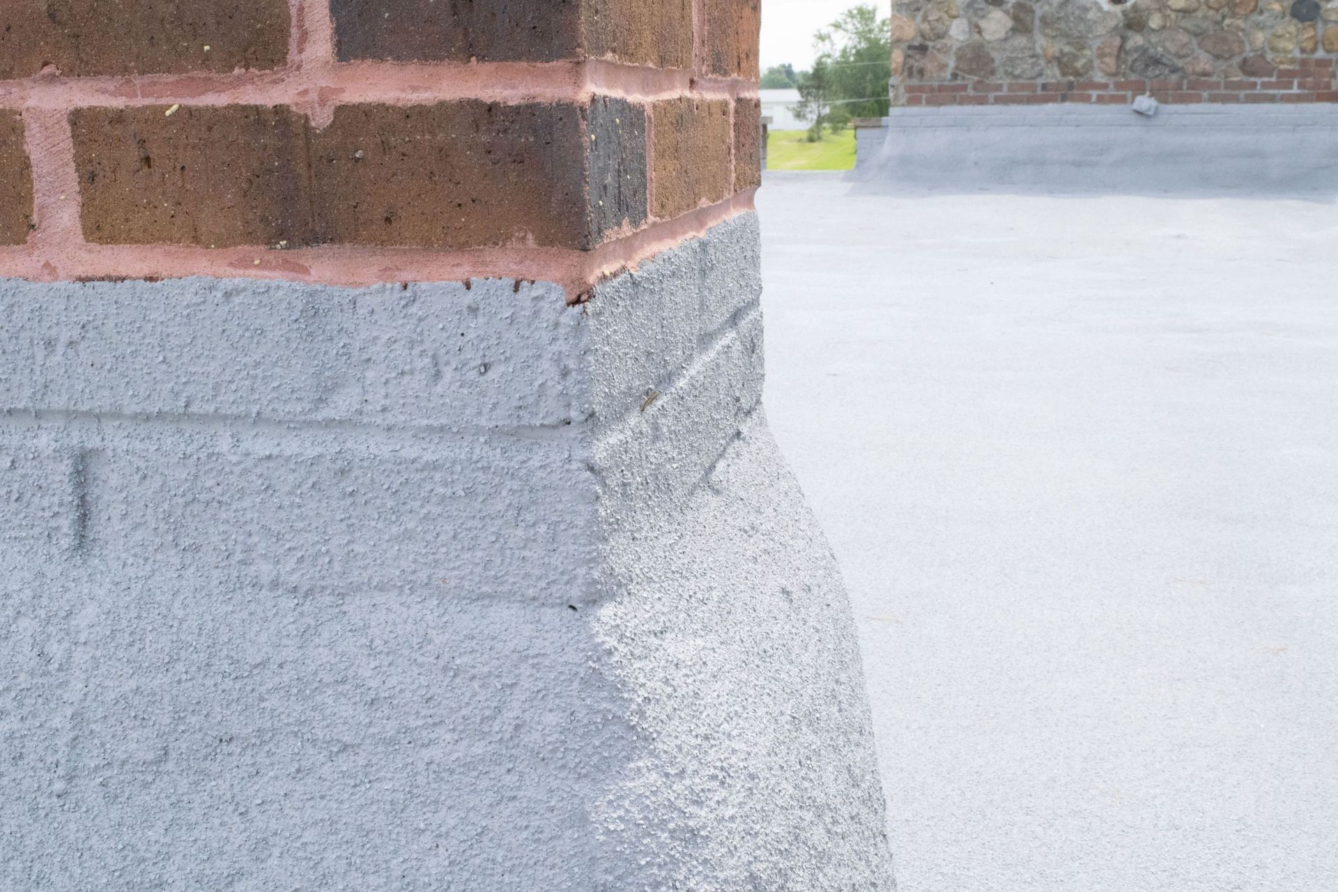 Brick building corner with gray stucco base beside a white rooftop or paved surface