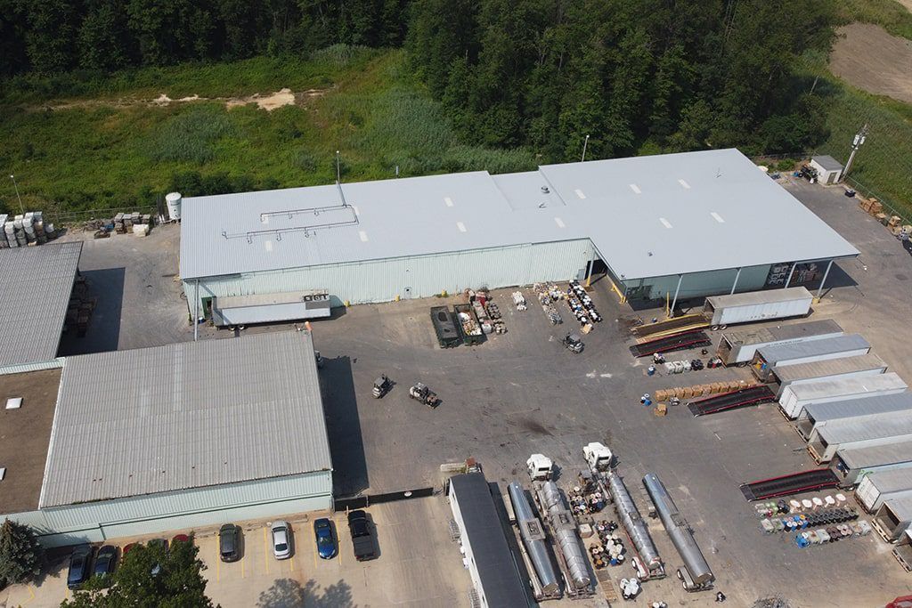 Aerial view of an industrial yard with long white warehouse buildings, trailers, and stacked materials.