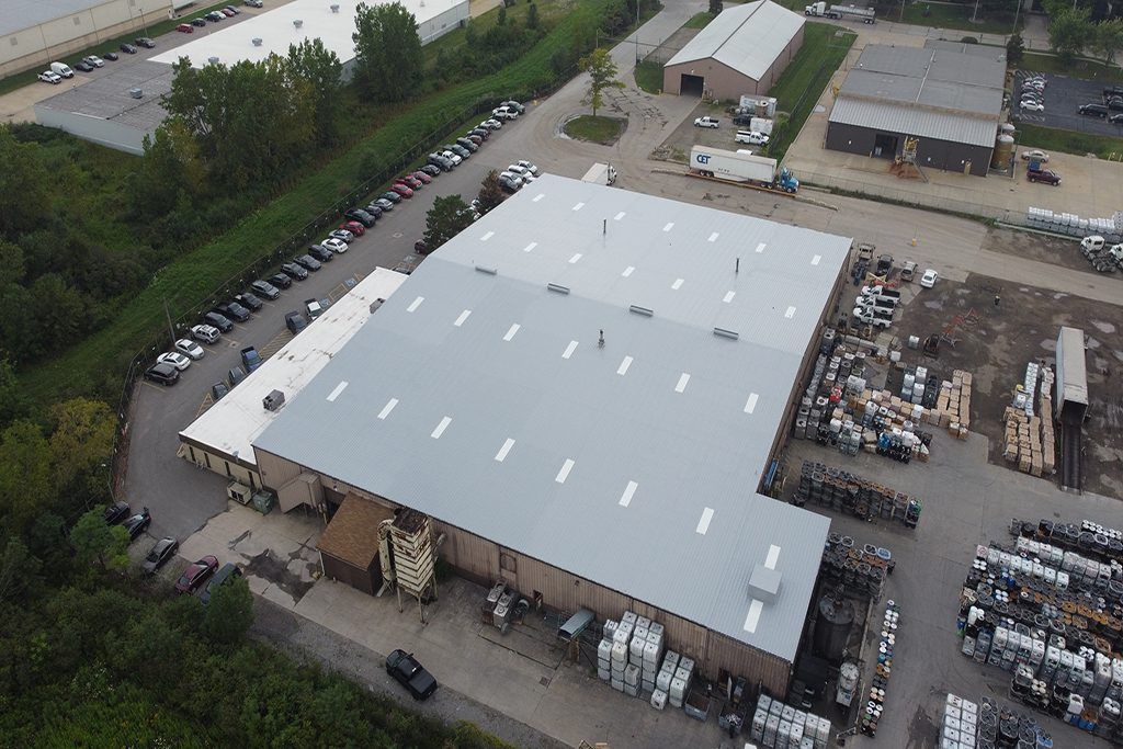 Aerial view of a large white-roofed warehouse with stacked pallets and parked trucks in an industrial yard